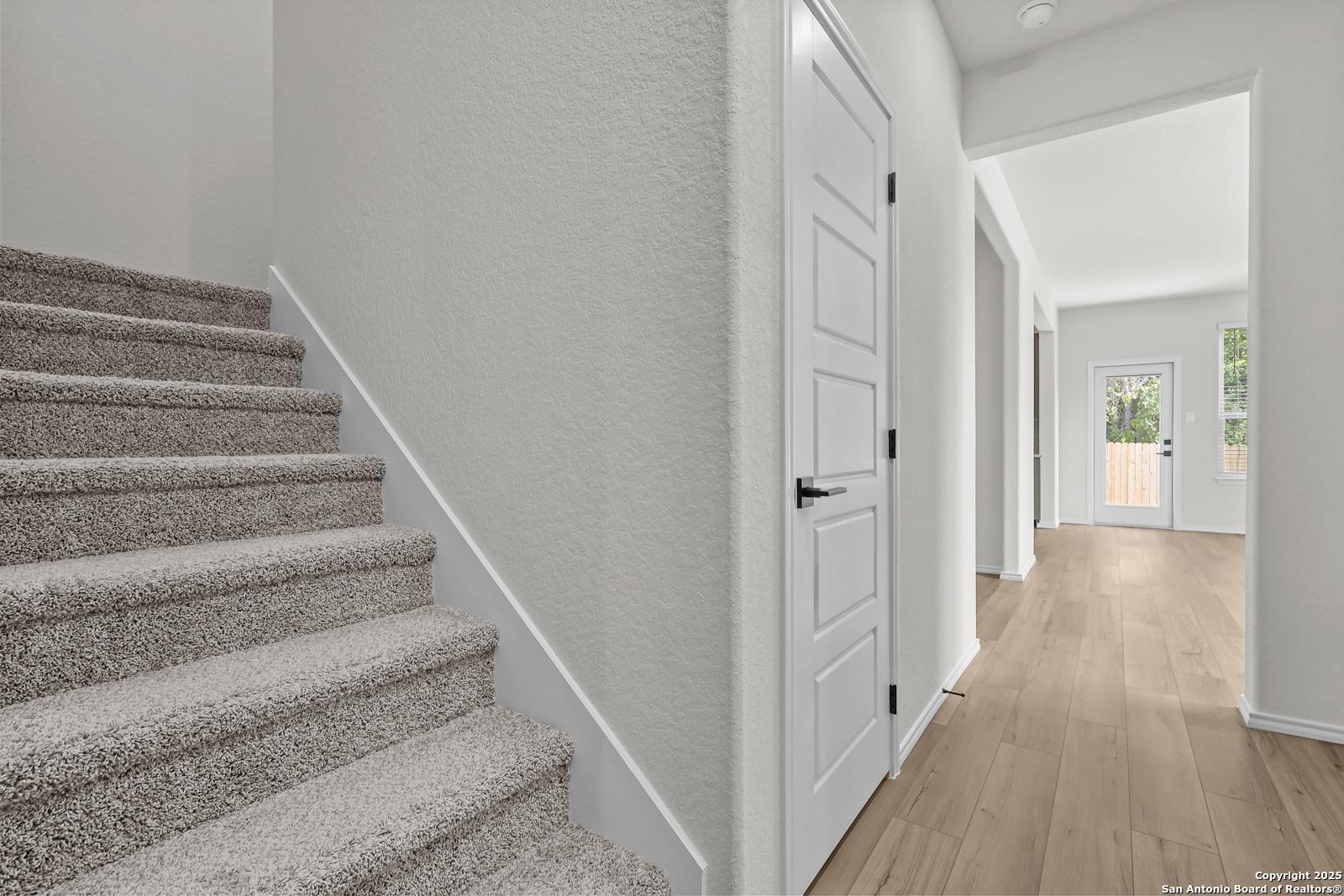 Carpeted staircase ascending to second floor beside open hallway with hardwood floors in The Florence C 2-story home, San Antonio