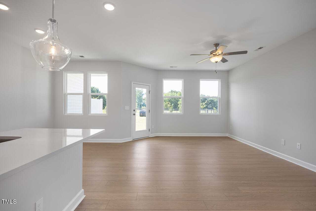 Open-concept kitchen-living space with white island sink, light wood floors, large windows, and ceiling fan in Davidson Homes The Graham, Fuquay-Varina, NC