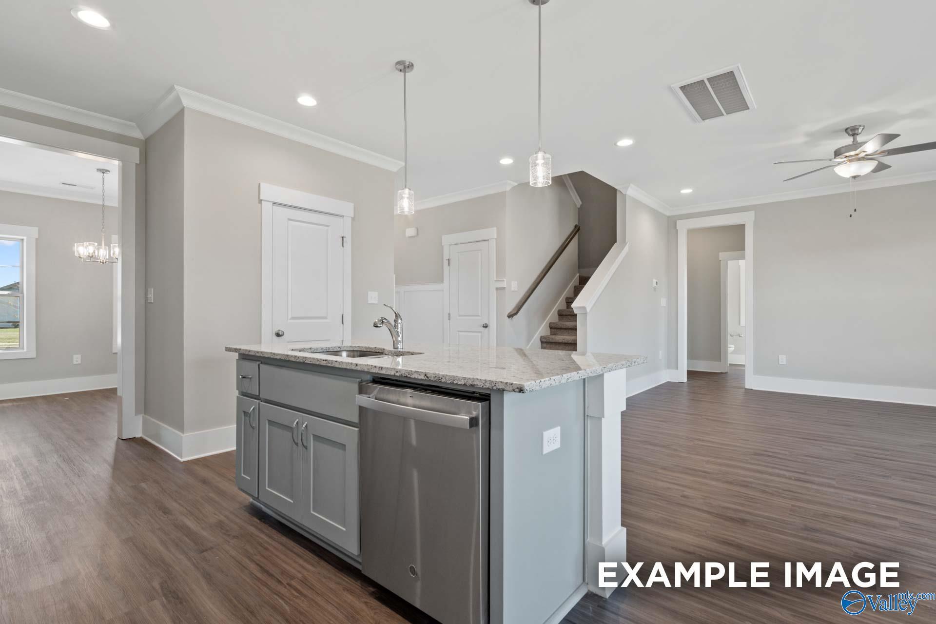Modern gray kitchen island with sink, dishwasher, and wood floors beside open staircase in Shelby B home, Huntsville, AL
