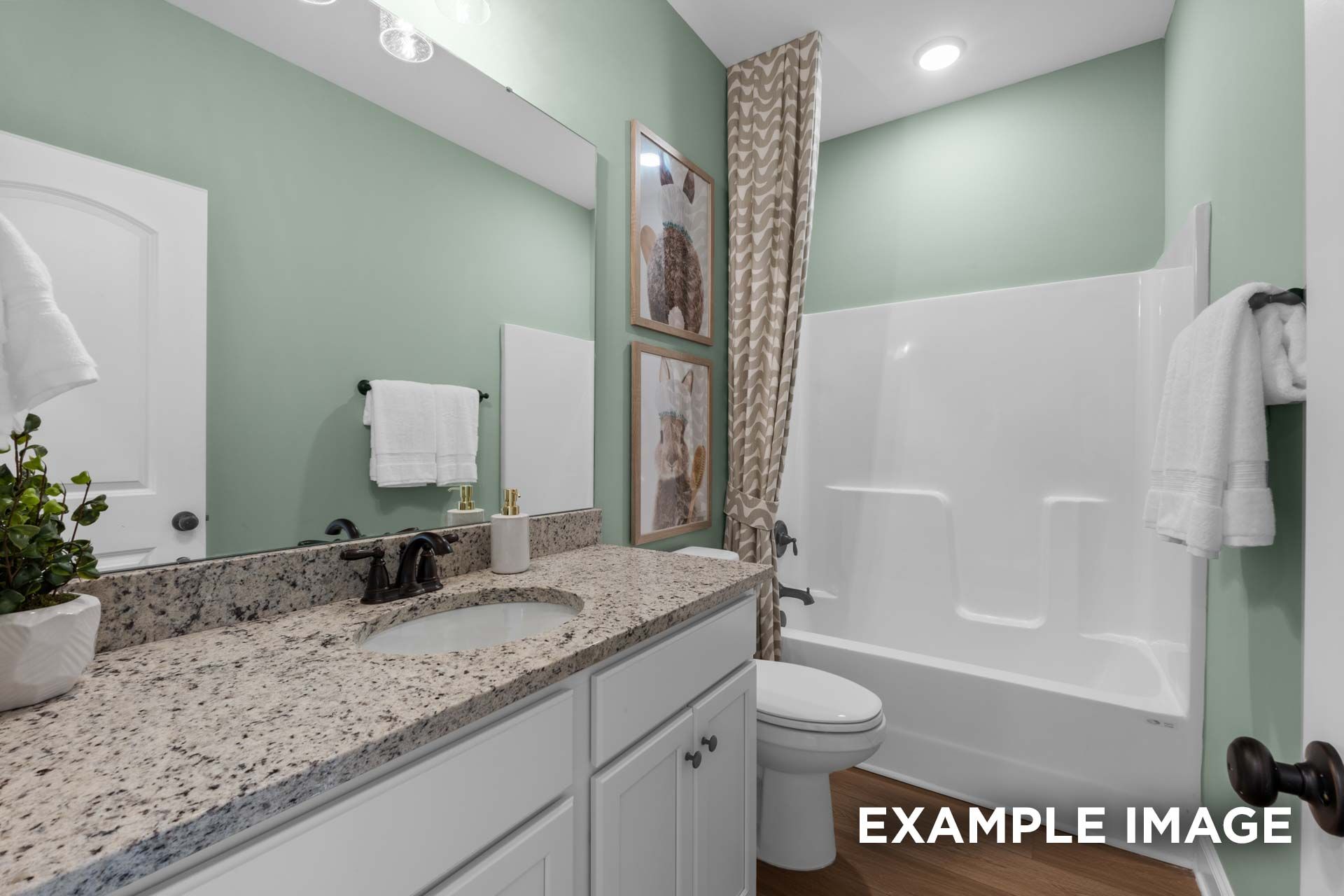 Spacious master bathroom in The Laurel N with seafoam green walls, granite double vanity, tub-shower combo, and framed art