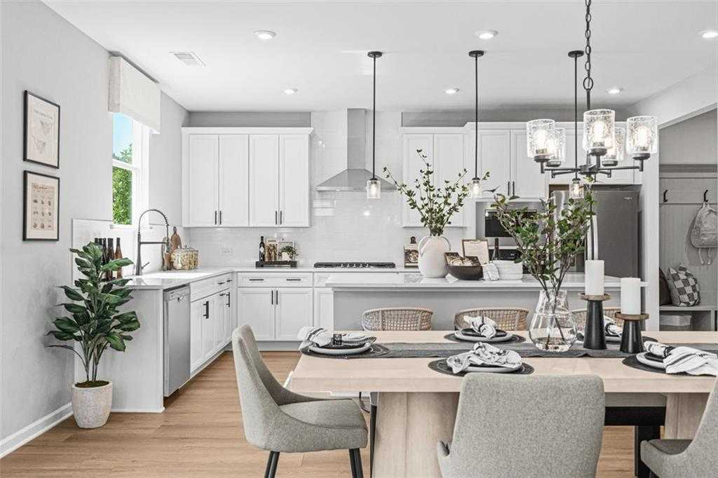 Bright open kitchen with white cabinets, stainless appliances, island sink, and wooden dining table in Davidson Homes The Hickory B, Hoschton, GA