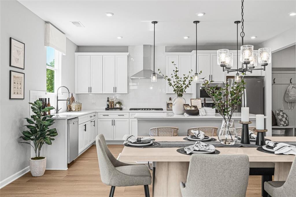 Bright open kitchen with white cabinets, stainless appliances, island sink, and wooden dining table in Davidson Homes The Hickory B, Hoschton, GA