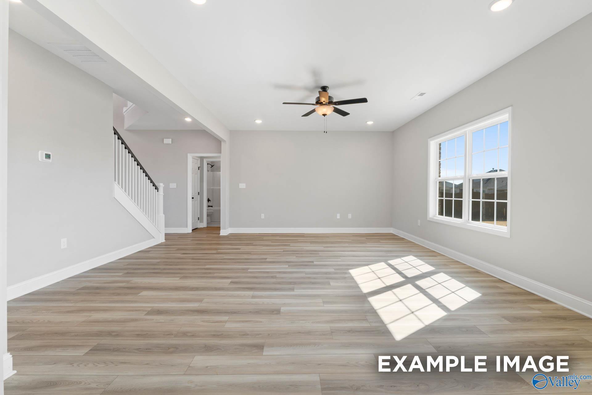 Spacious, open-concept living area with light wood-style flooring in The Madison D floor plan at Evergreen Mill, Madison.