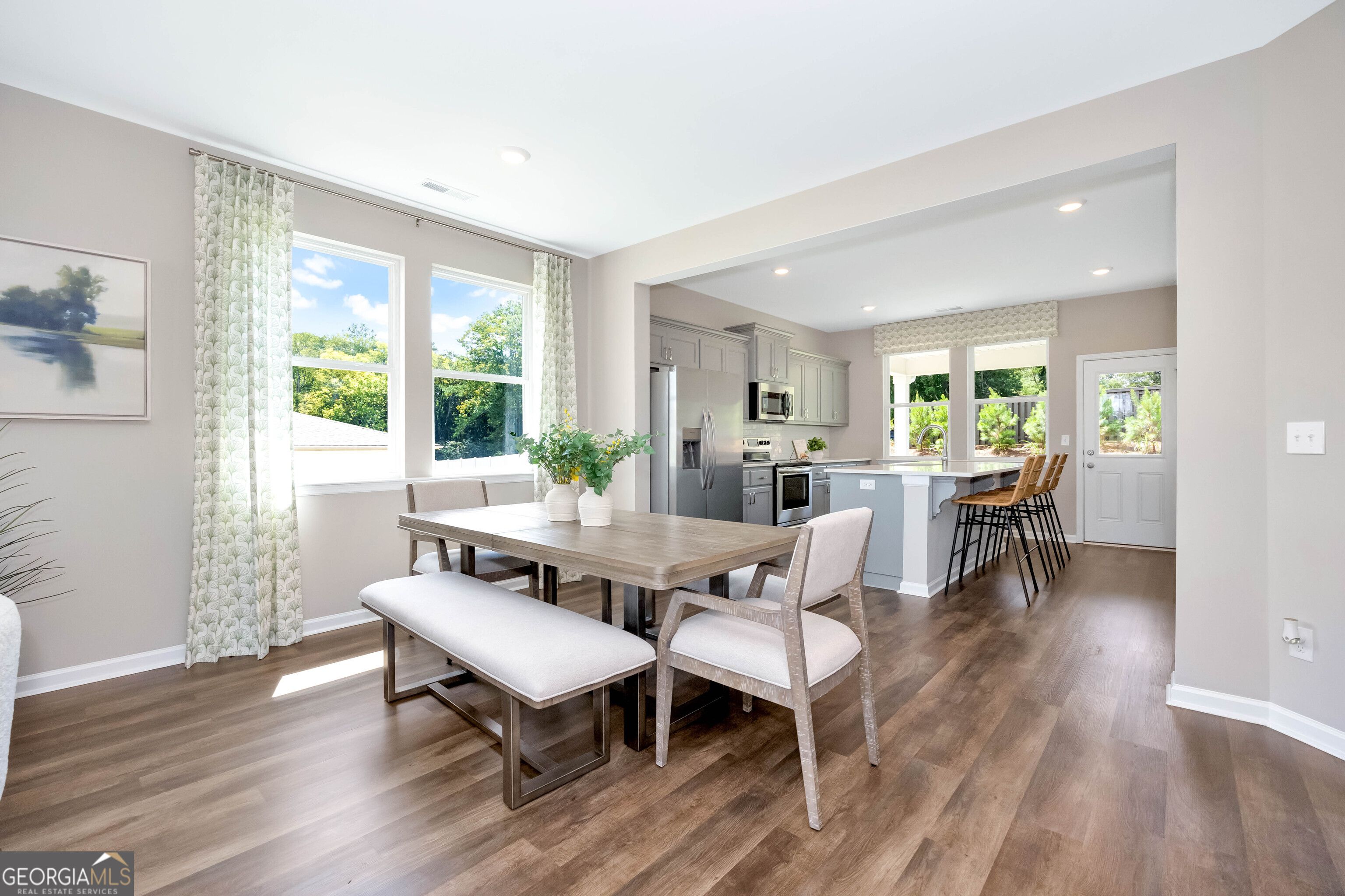 Bright open dining area with wooden table, bench, and chairs adjacent to modern kitchen island in Evermore Homes The Stella, Perry, Georgia