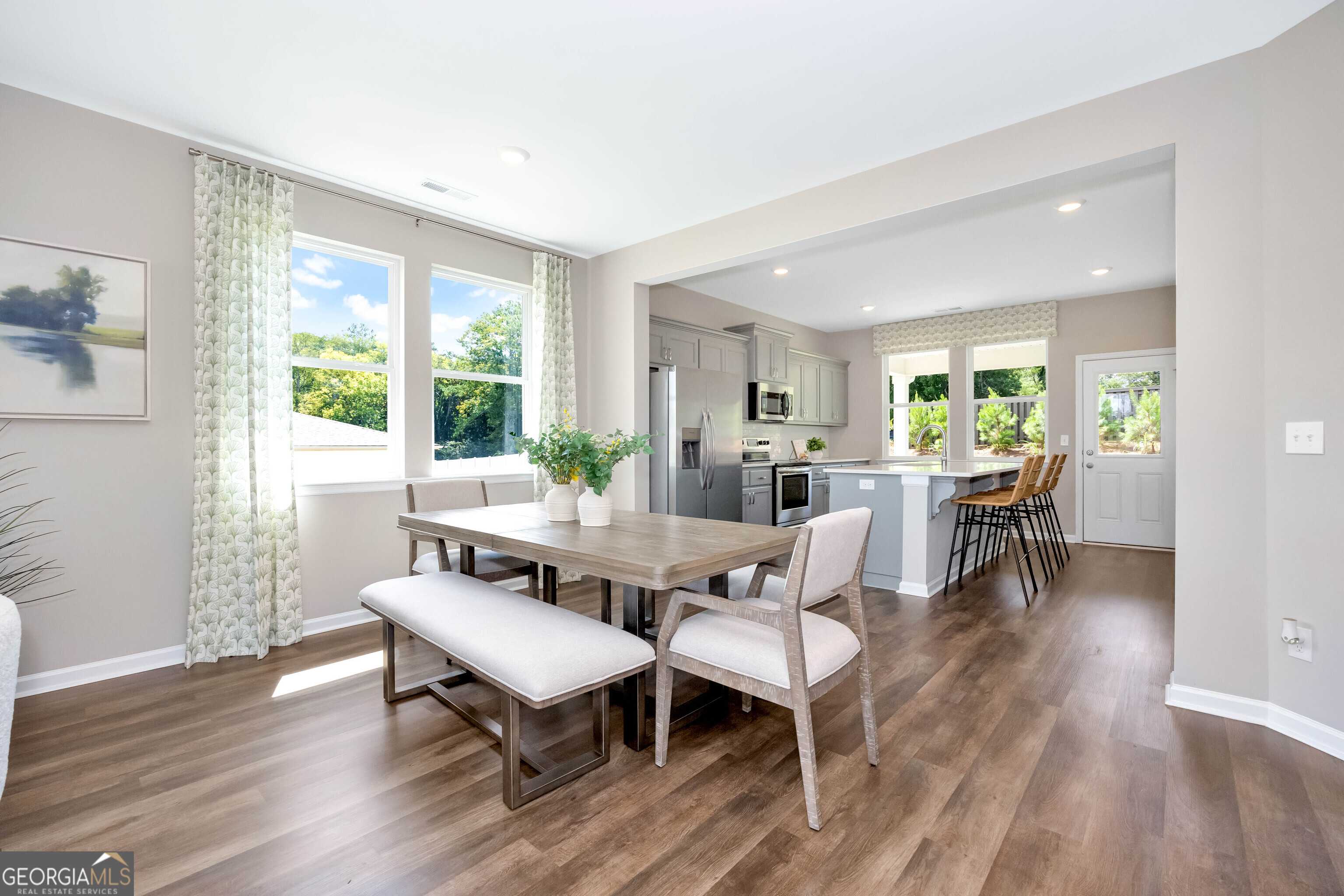 Bright open dining area with wooden table, bench, and chairs adjacent to modern kitchen island in Evermore Homes The Stella, Perry, Georgia