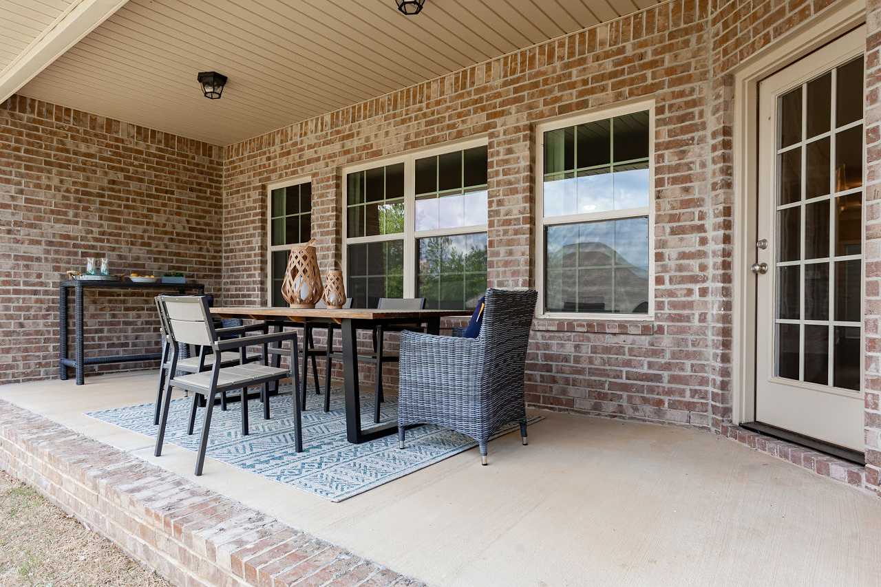 Spacious covered porch of The Rockford home featuring brick walls, French doors, metal dining table, wicker chairs, and recessed lighting