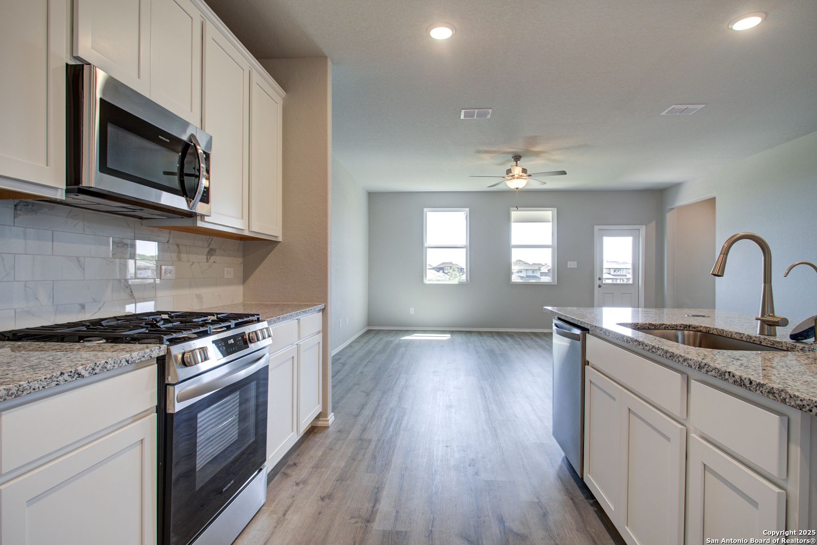 Open-concept kitchen with white cabinets, granite counters, stainless appliances in The Douglas G home, Comanche Ridge, San Antonio