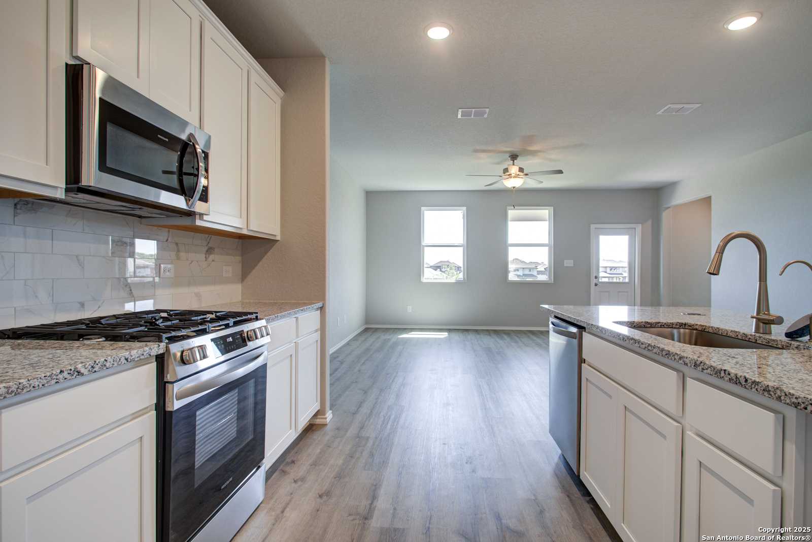 Open-concept kitchen with white cabinets, granite counters, stainless appliances in The Douglas G home, Comanche Ridge, San Antonio