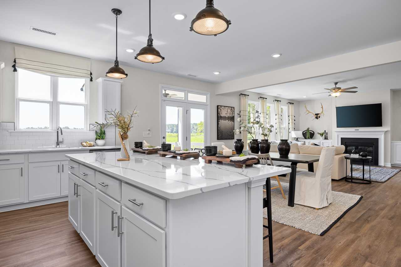 Open-concept kitchen and living room at Wellers Knoll in Lillington NC with white cabinets, quartz island, pendant lights and hardwood floors