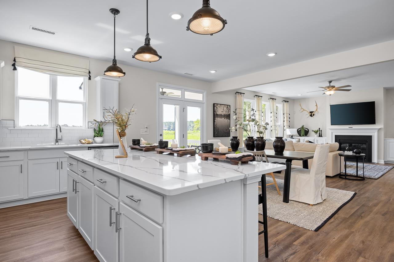 Open-concept kitchen and living room at Wellers Knoll in Lillington NC with white cabinets, quartz island, pendant lights and hardwood floors