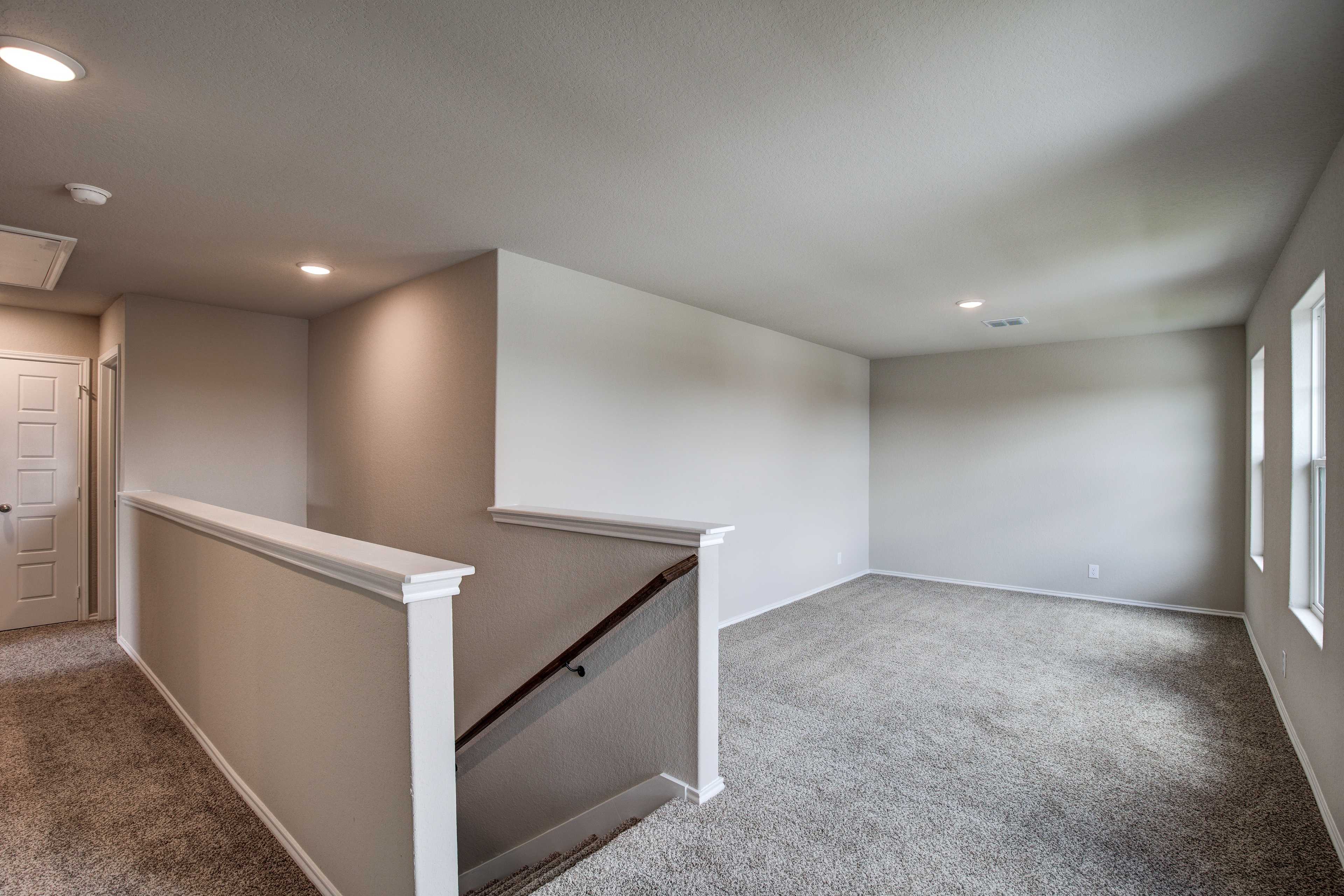 Upper floor hallway in The Murray 2-story home with beige walls, carpeted floors, staircase railing, and adjacent empty rooms