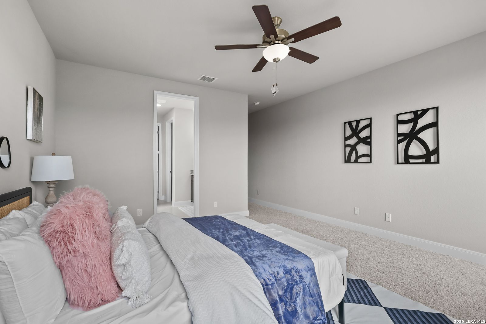 Spacious master bedroom with ceiling fan, plush king bed, abstract art, and en-suite access in Davidson Homes The Rockford G, Ladera, San Antonio
