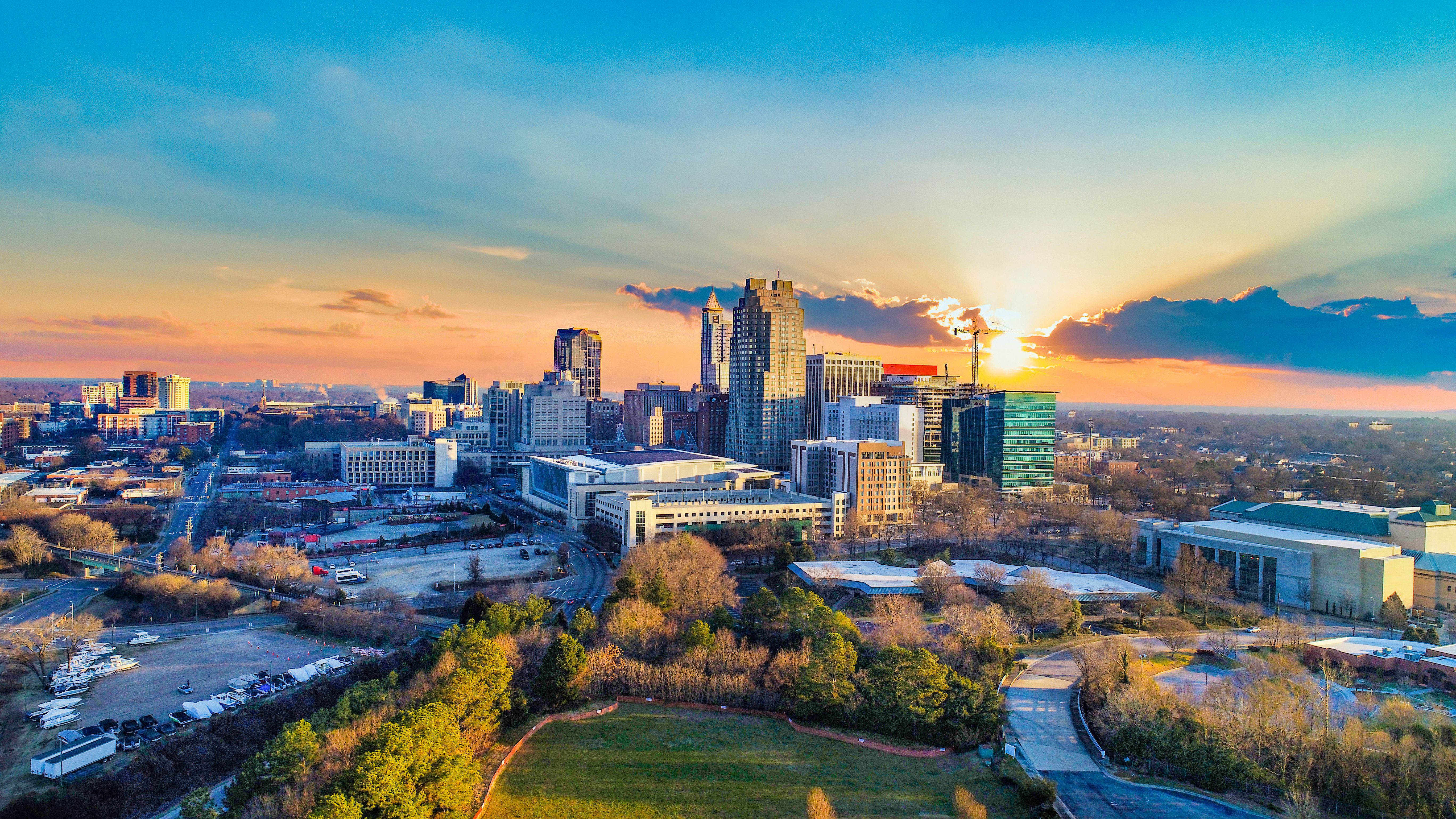 Aerial sunset view of Raleigh skyline near Forestville Yard Townhomes in Knightdale NC with modern towers and green parks