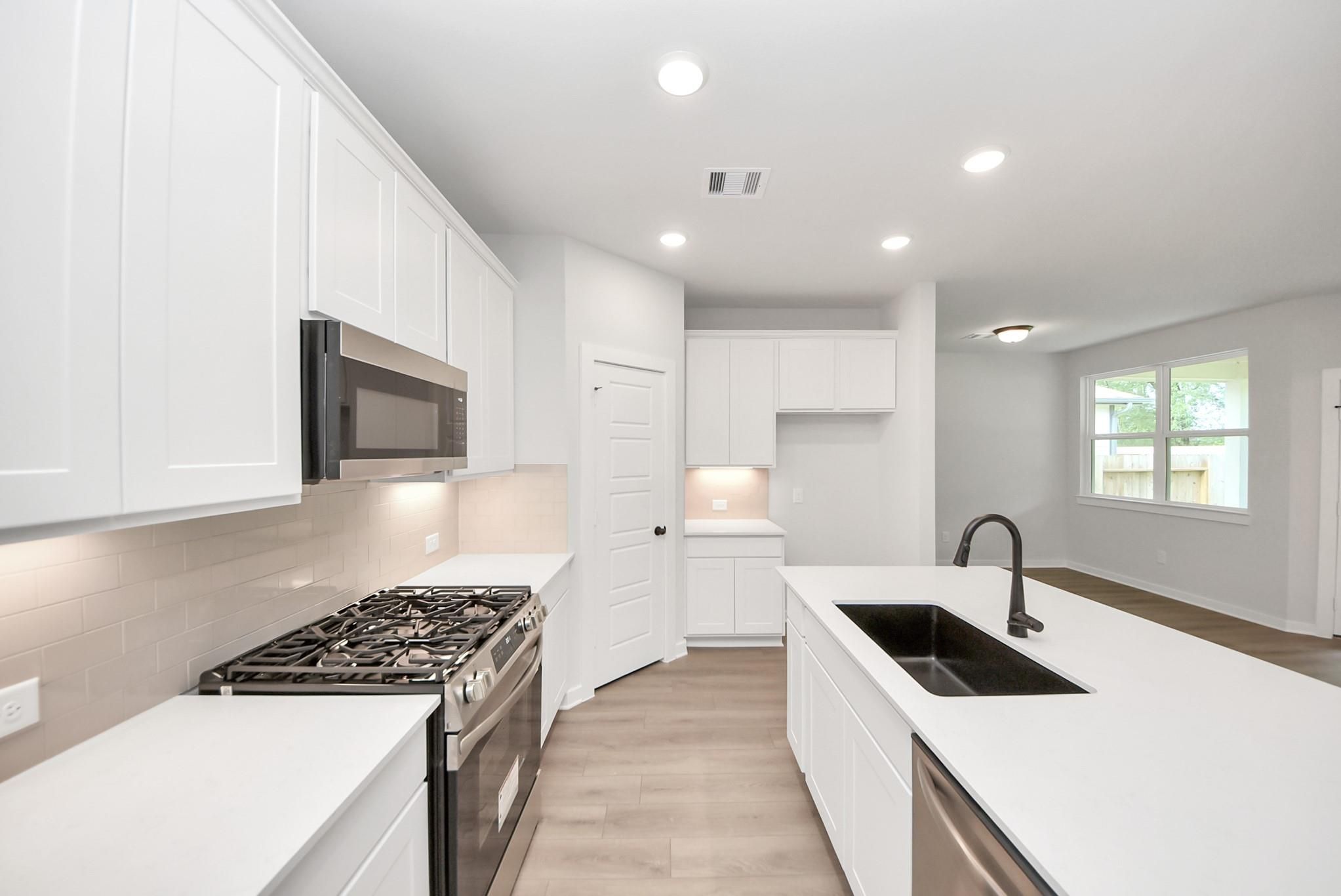 Modern kitchen with white cabinets, island, and stainless appliances in The Daphne F floor plan, Sundance Cove, Crosby TX.