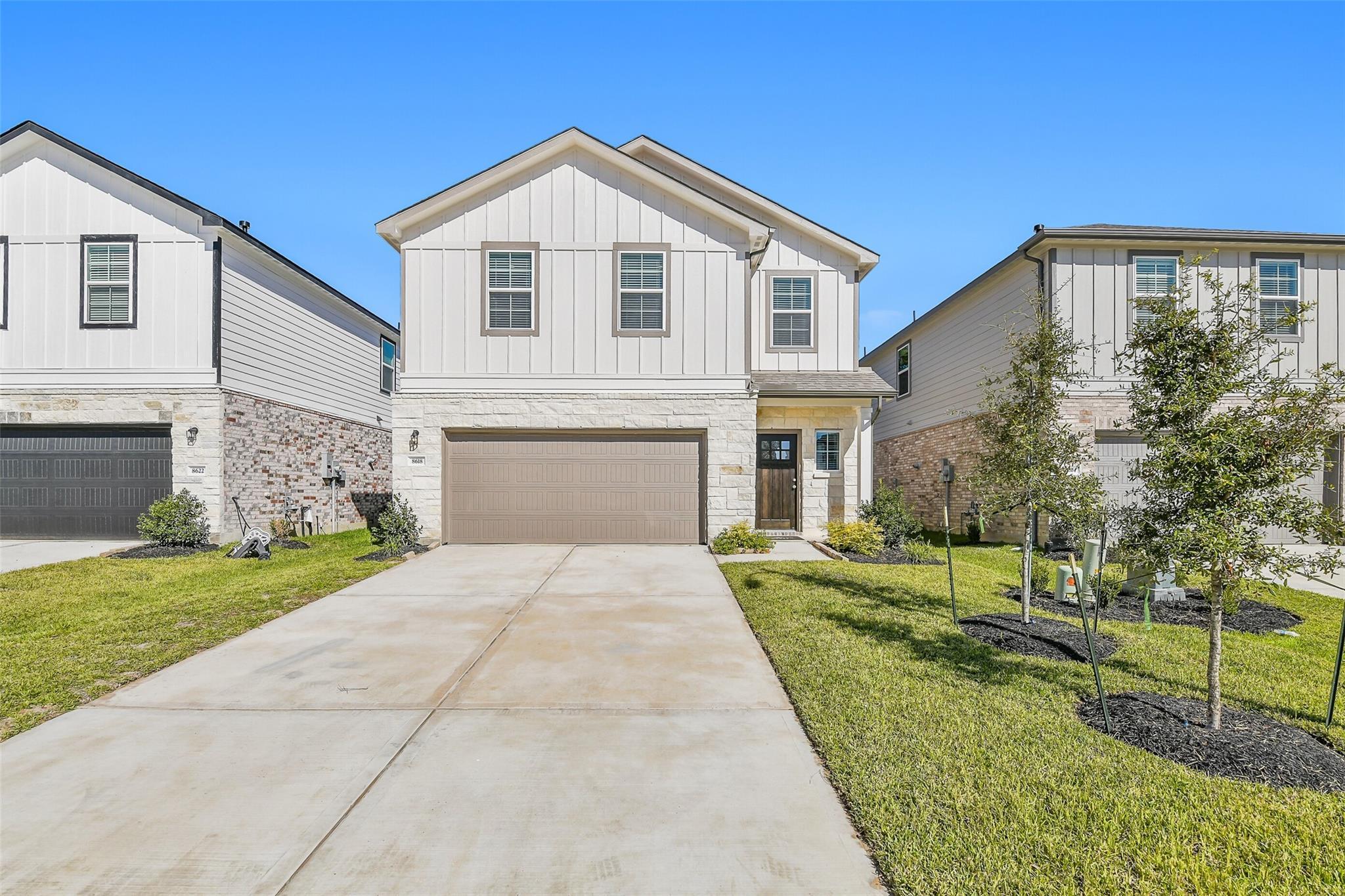 Modern two-story Davidson Homes Blanco E with white siding, stone accents, two-car garage, driveway, and lush lawn in Lakes at Black Oak, Magnolia, Texas