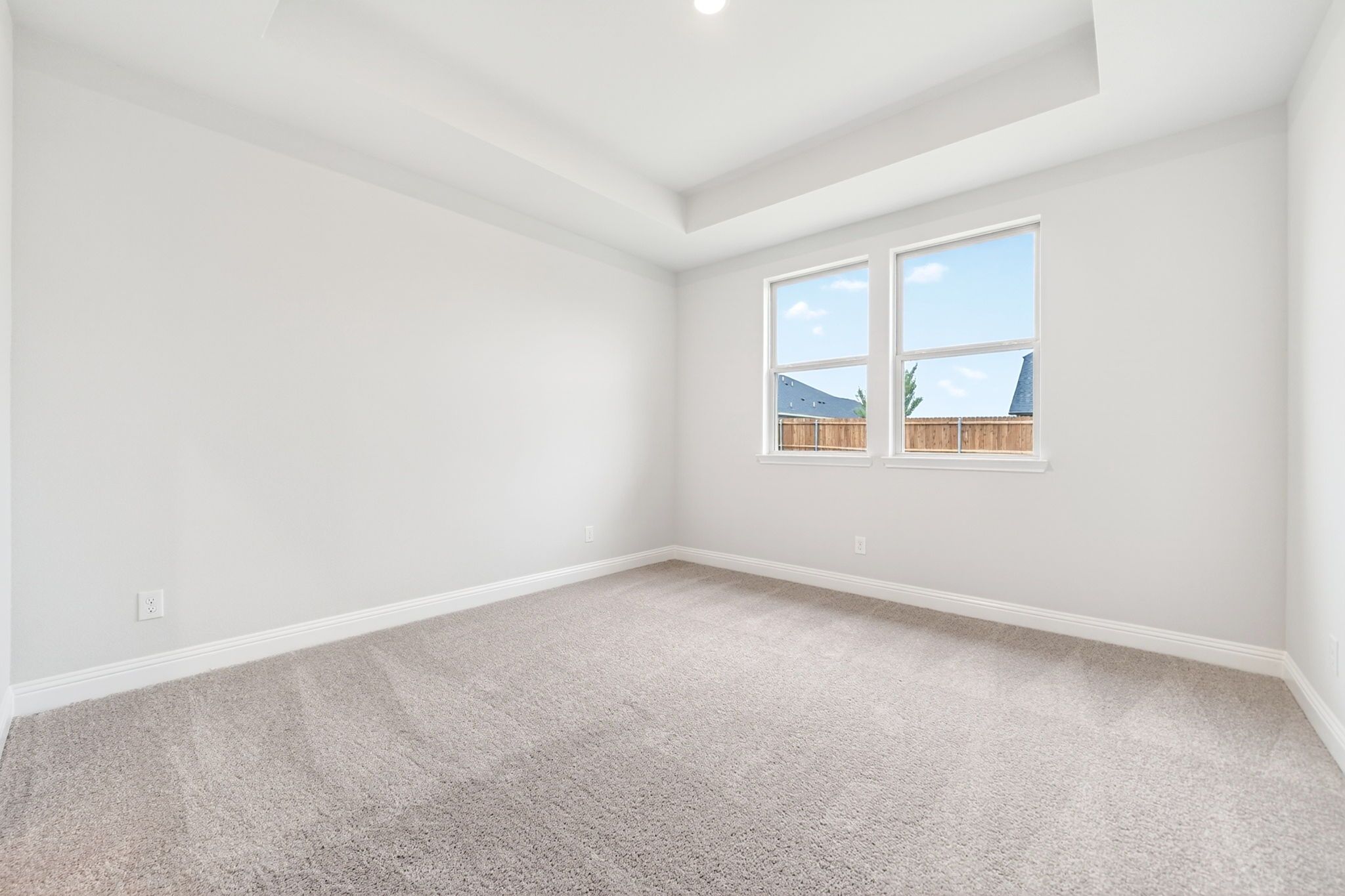 Bright bedroom with plush carpet and tray ceiling in The Redbud A single-family home design by Davidson Homes.