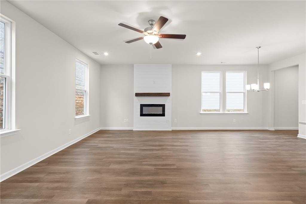 Cozy living room with white brick gas fireplace, hardwood floors, ceiling fan, and large windows in Davidson Homes The Marion B, Kennesaw, Georgia