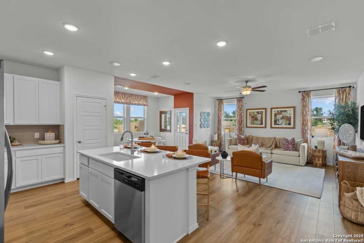 Open-concept kitchen and living area with white island sink, hardwood floors, orange accents in Davidson Homes The Daphne J, Elmendorf, Texas