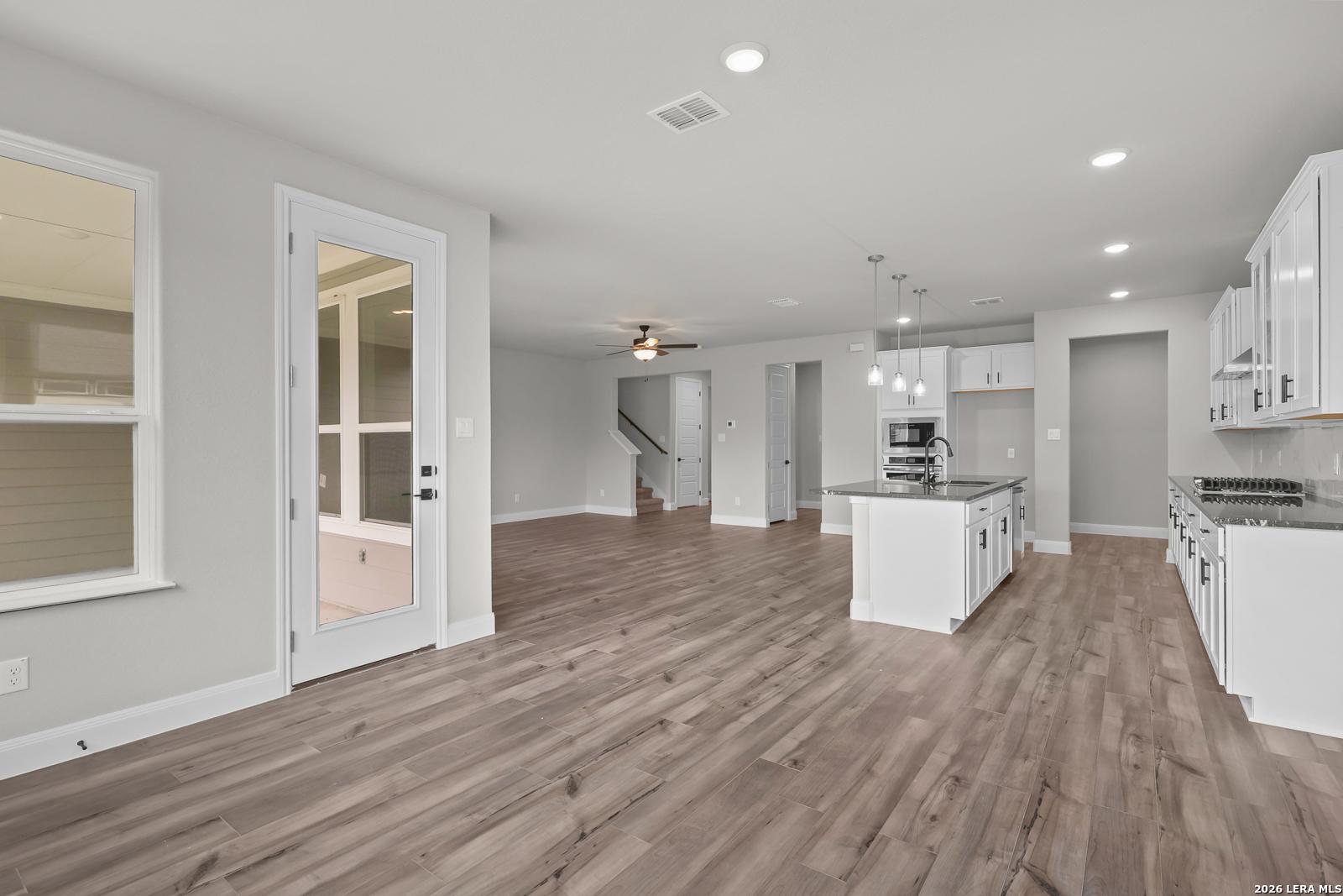 Open-concept kitchen with white cabinets, granite island, stainless appliances, and hardwood floors in The Belmont H, Castroville, Texas
