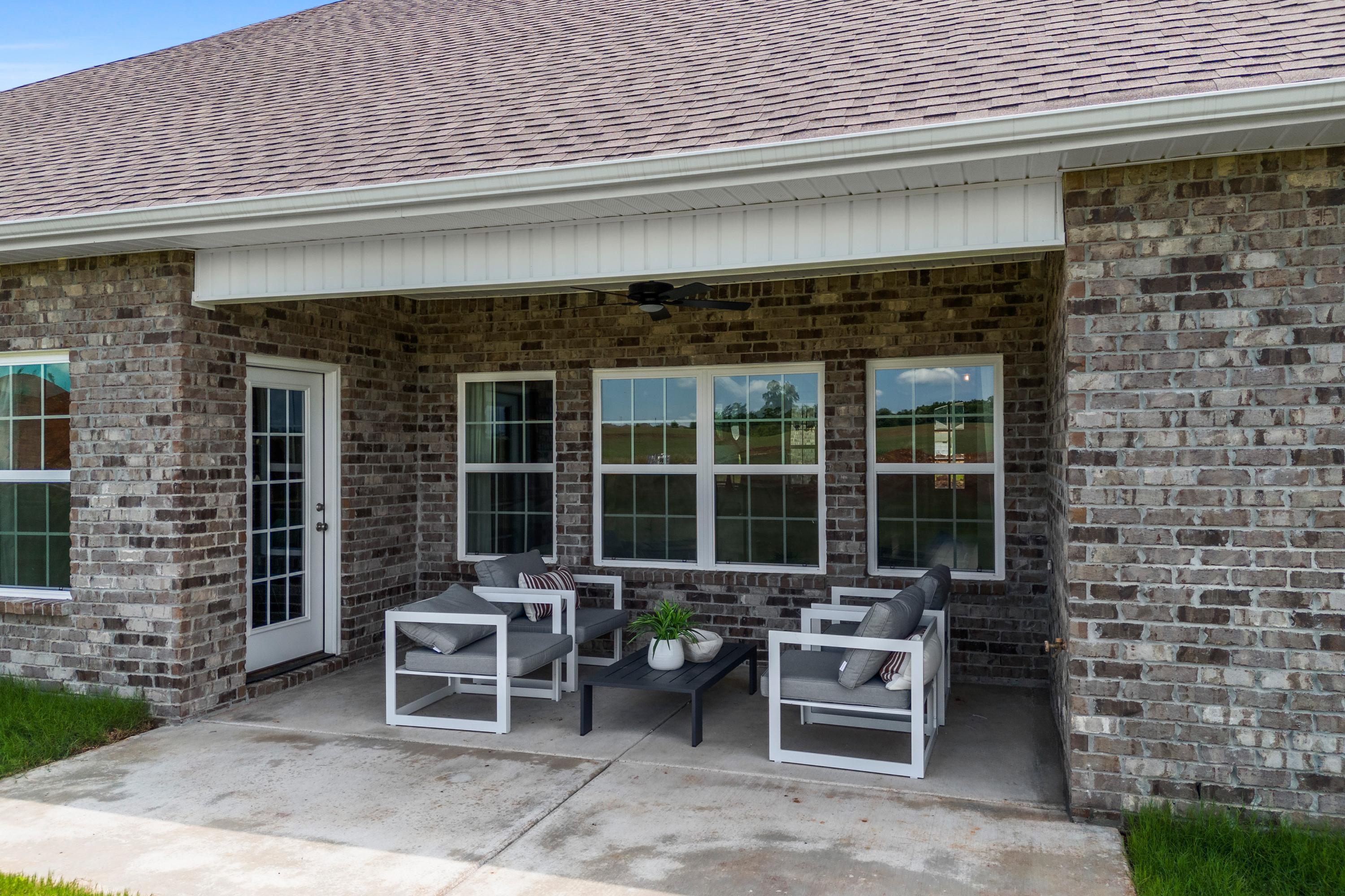 Covered patio at Creekside in Harvest AL by Davidson Homes with brick exterior, ceiling fan, white outdoor seating and potted plant