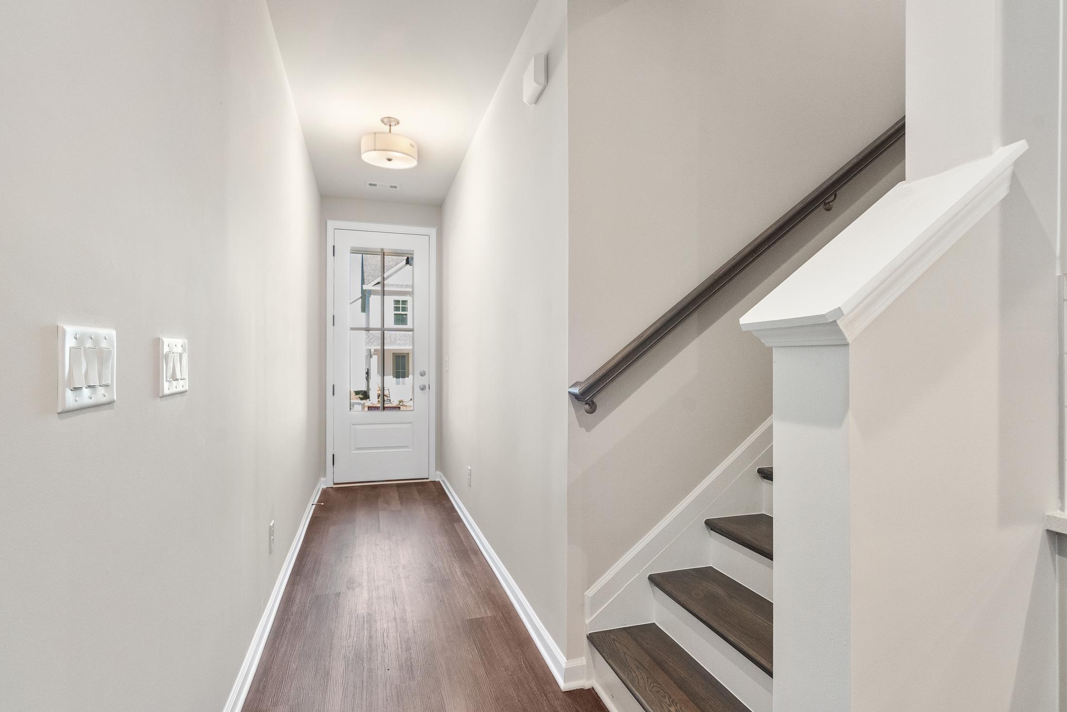 Spacious upper-floor hallway in The Cary B home design with dark wood floors, white staircase railing, and glass-paneled door