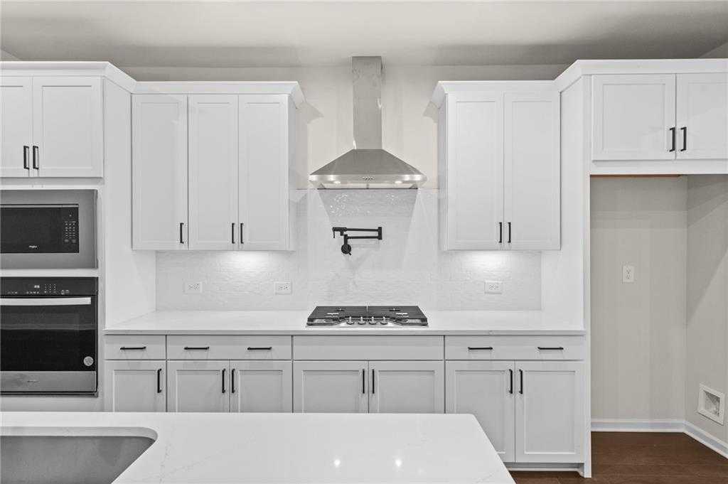 Modern white kitchen with stainless steel gas range, quartz island, and shaker cabinets in The Glenwood A, Loganville, GA