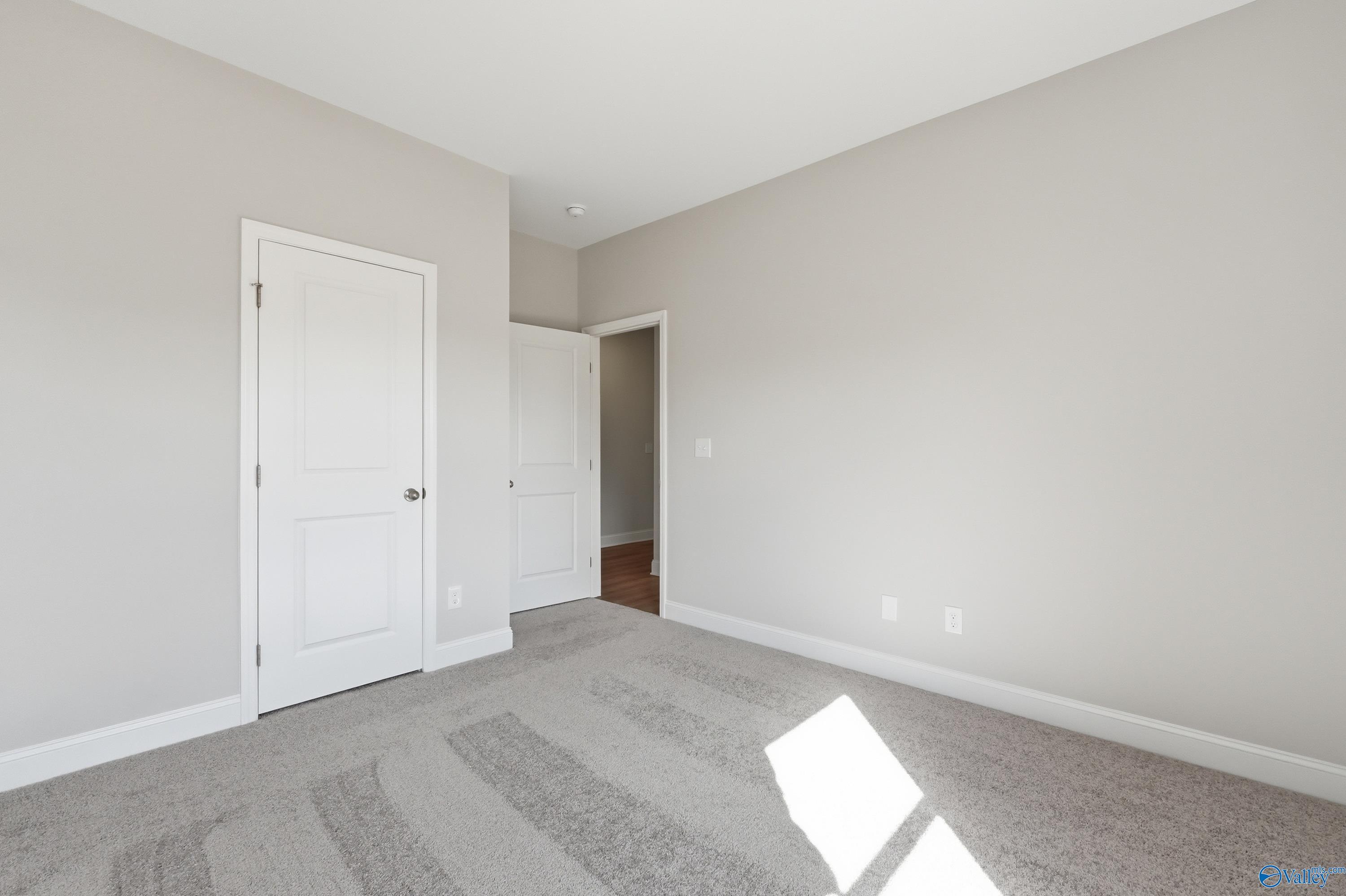 Bright secondary bedroom with neutral gray walls, plush carpet, white doors, and adjacent bath in Davidson Homes Asheville C, Huntsville AL