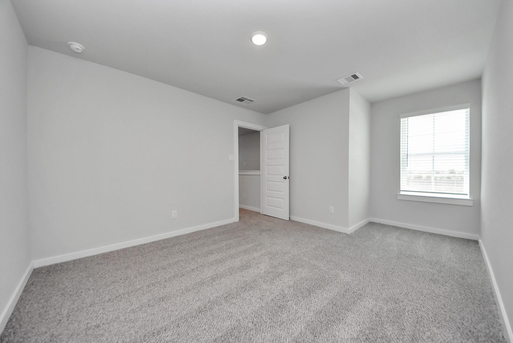 Bright empty bedroom with gray carpet and white walls in Davidson Homes The San Marcos E, Emberly, Beasley, Texas
