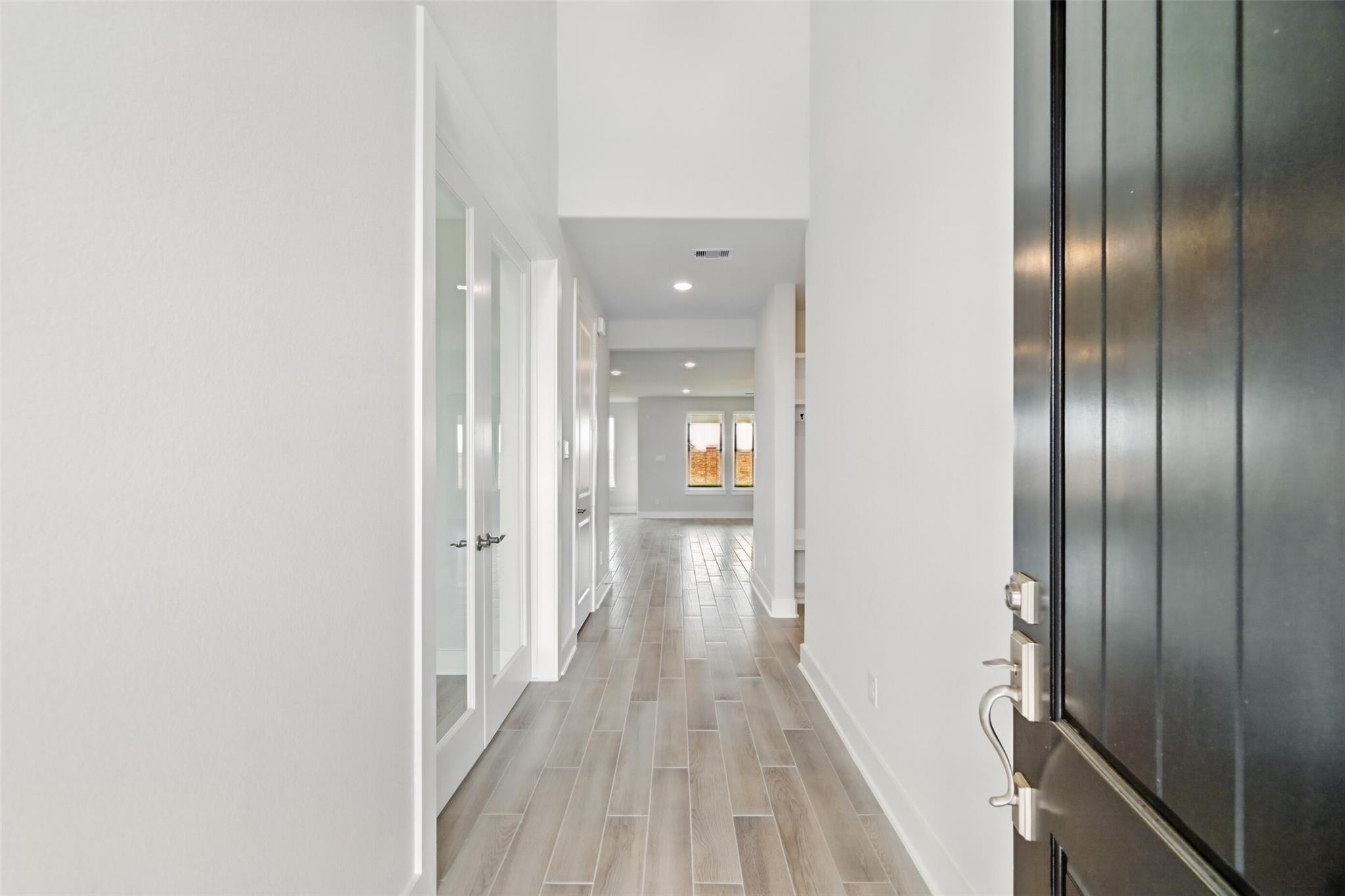 Spacious hallway with white walls, luxury plank flooring, and glass doors in Davidson Homes The Philip A, Lago Mar, Texas City
