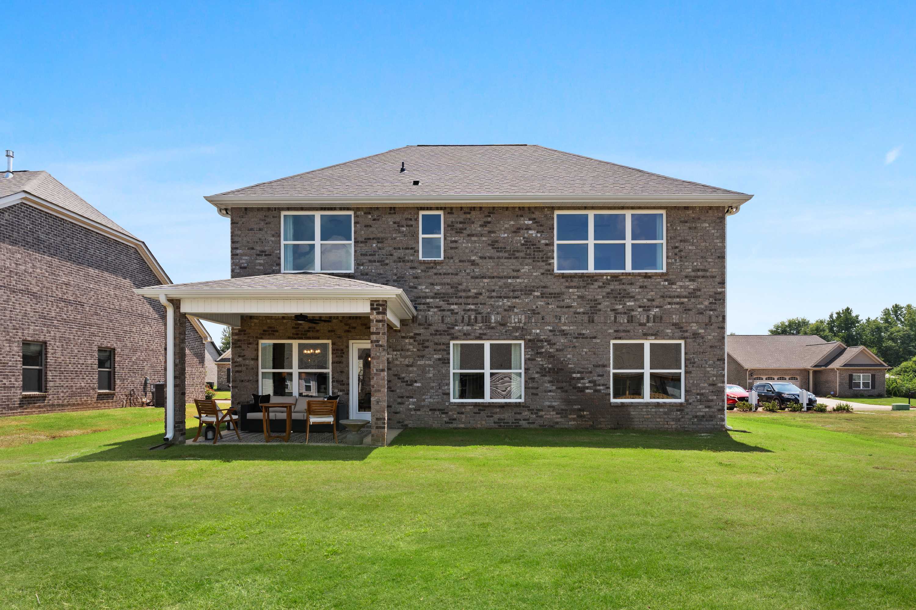 Brick two-story home backyard at Ricketts Farm in Athens, Alabama with covered patio, outdoor seating, and lush green lawn