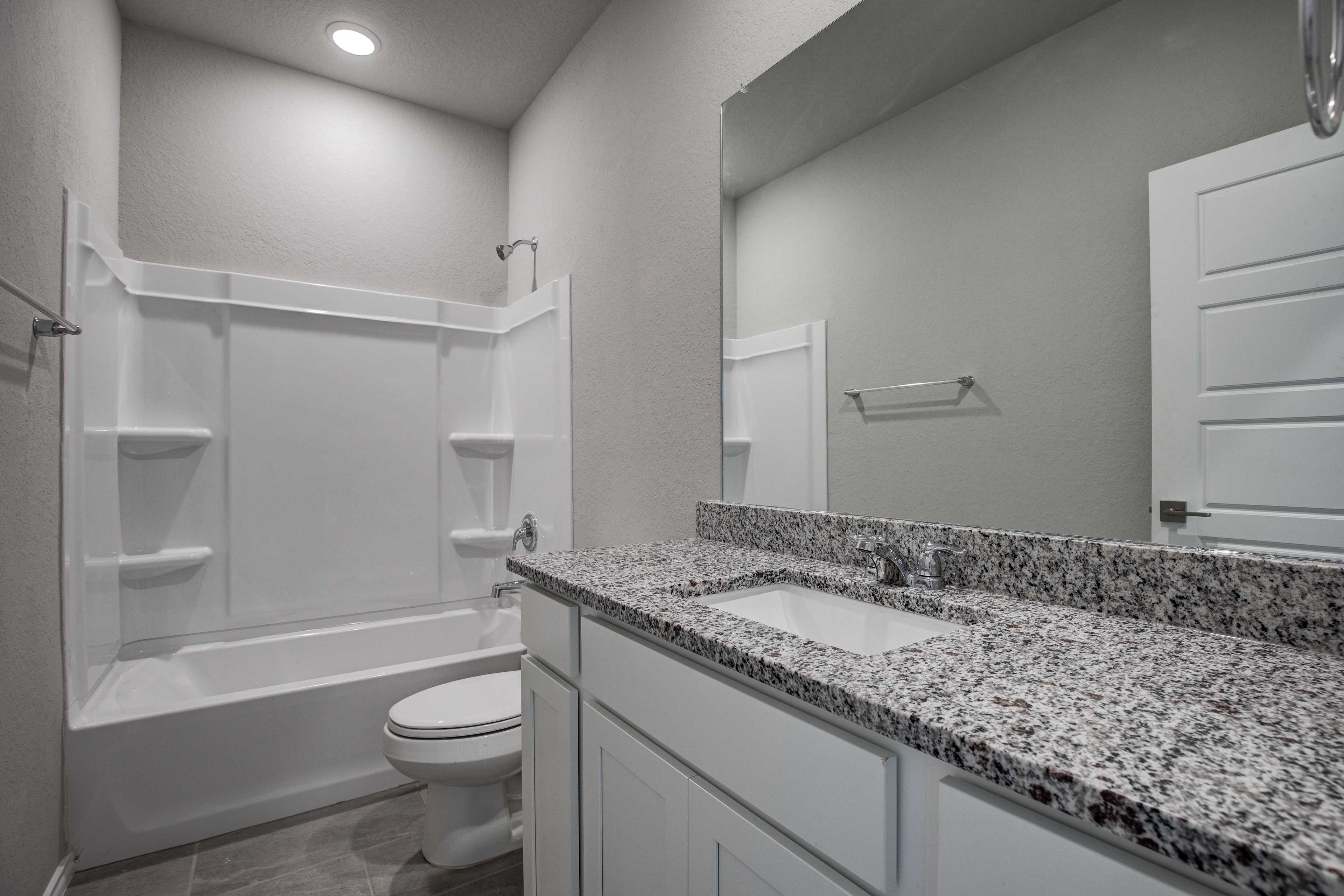 Spacious master bathroom in The Asheville home: white tub-shower combo, granite vanity with sink, large mirror, gray walls
