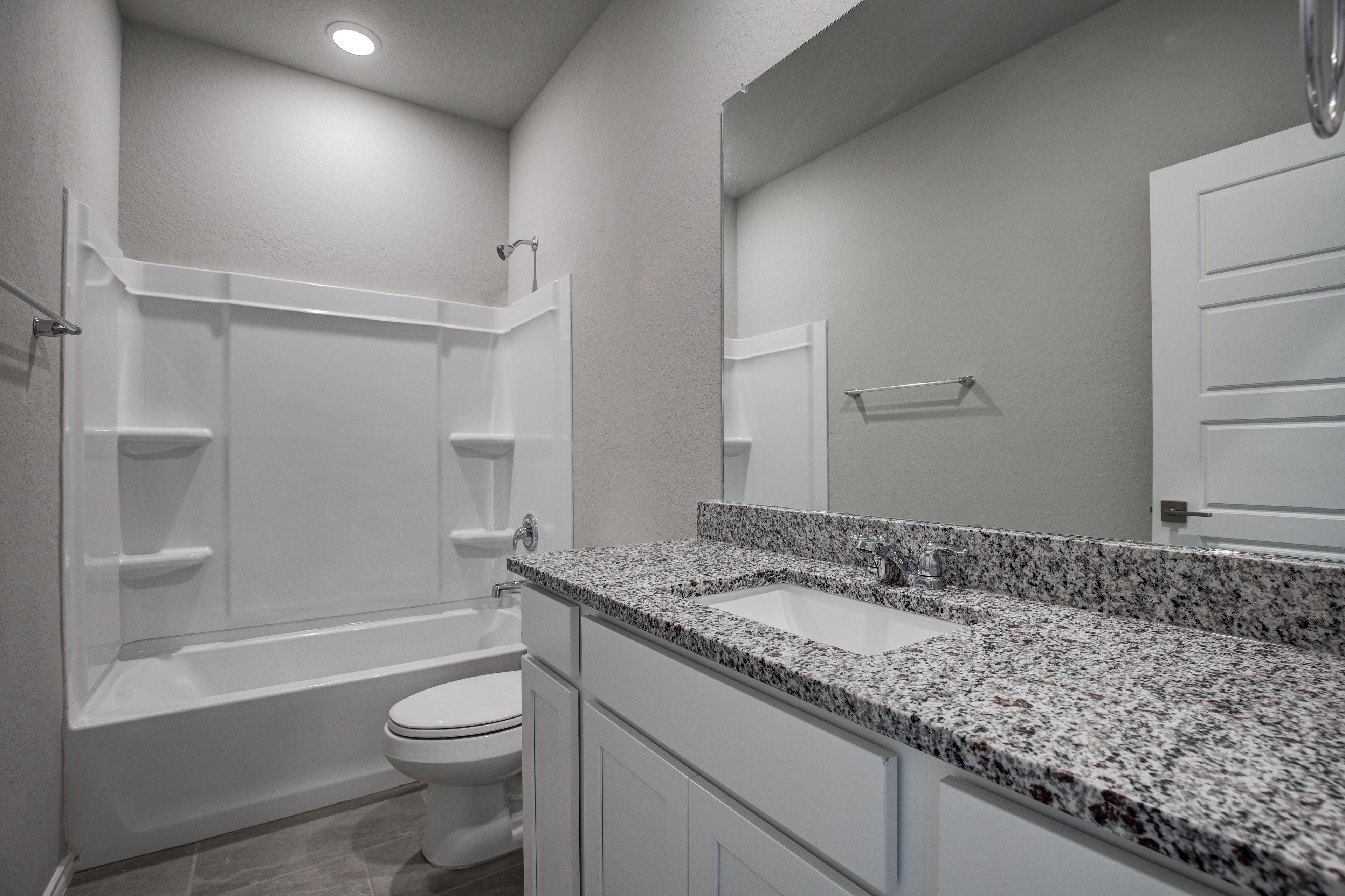 Contemporary bathroom in The Asheville by Davidson Homes featuring granite vanity, white tub-shower combo, and sleek fixtures
