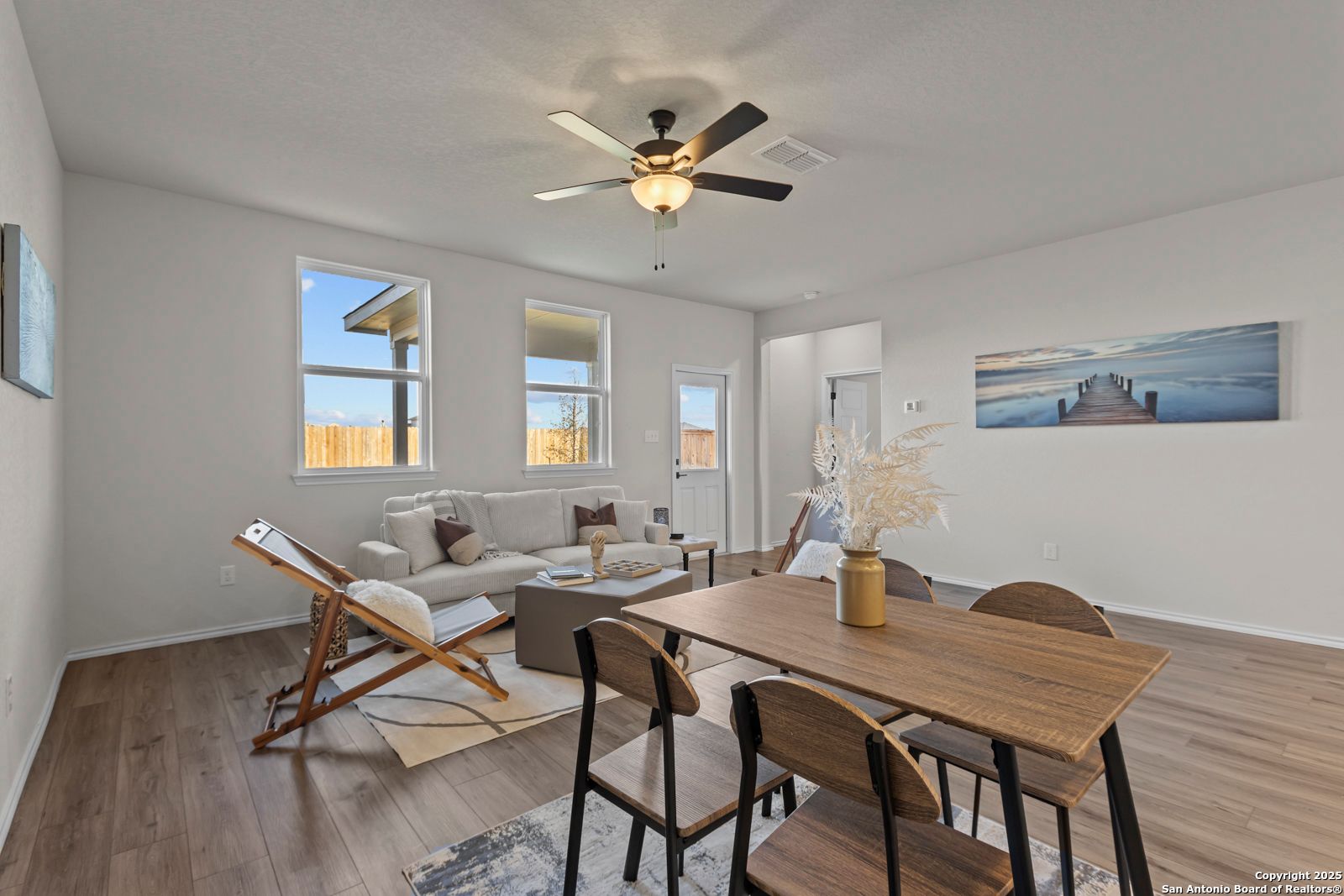 Bright open living-dining area with beige sofa, wooden table, ceiling fan in 3-bed Davidson Homes Douglas C, Seguin TX