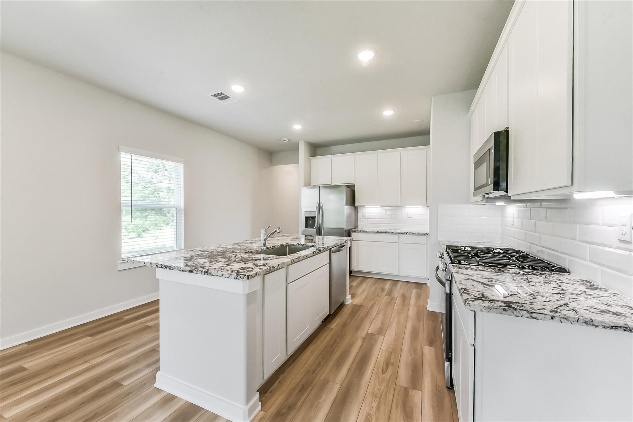 Contemporary kitchen with granite countertops, white cabinets, stainless appliances in Davidson Homes The Frio G, Magnolia Texas