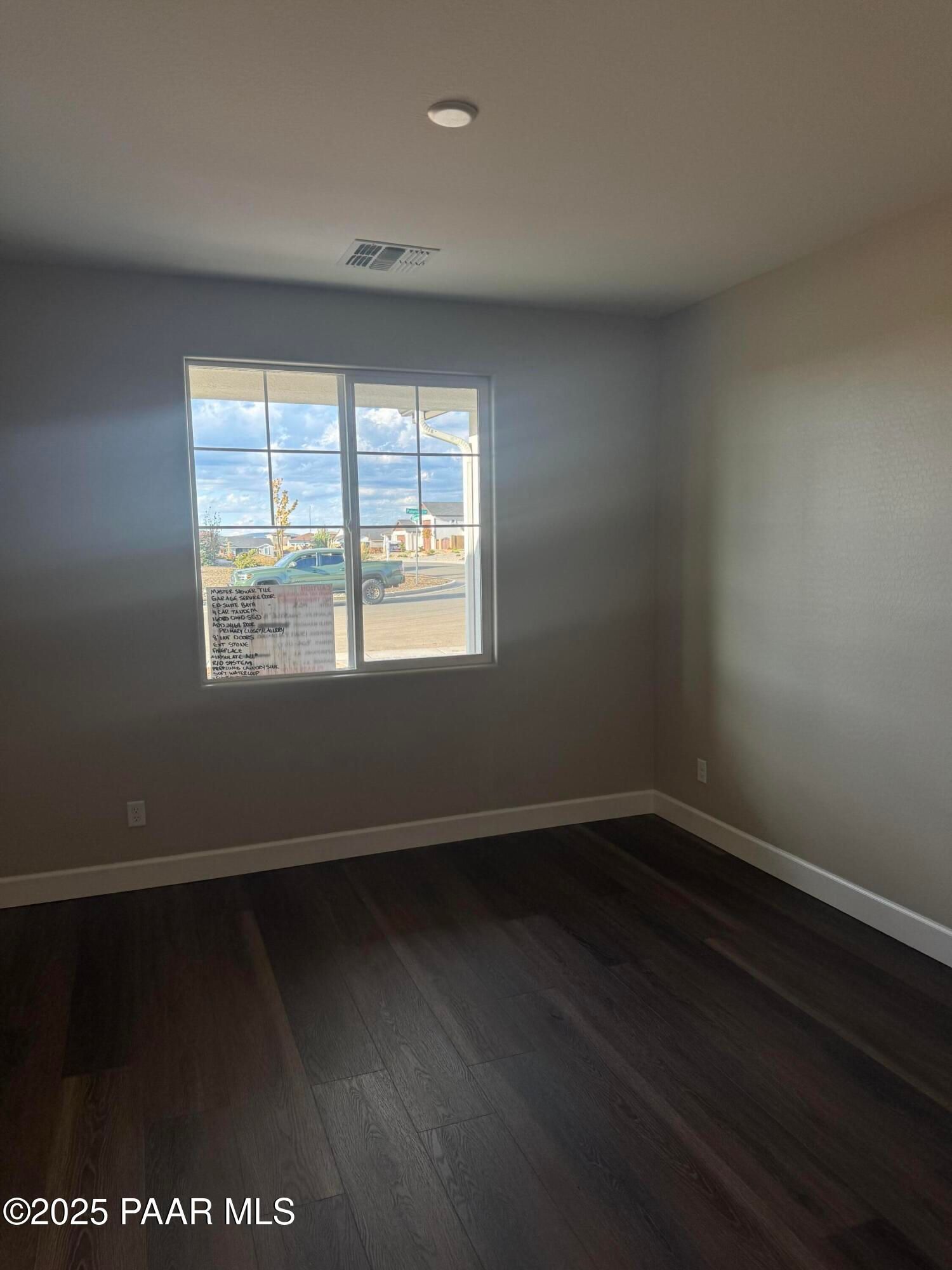 Bright bedroom featuring hardwood floors, neutral walls, and large grid window with sunny outdoor view in Evermore Homes The Sunrise A, Prescott Valley, Arizona