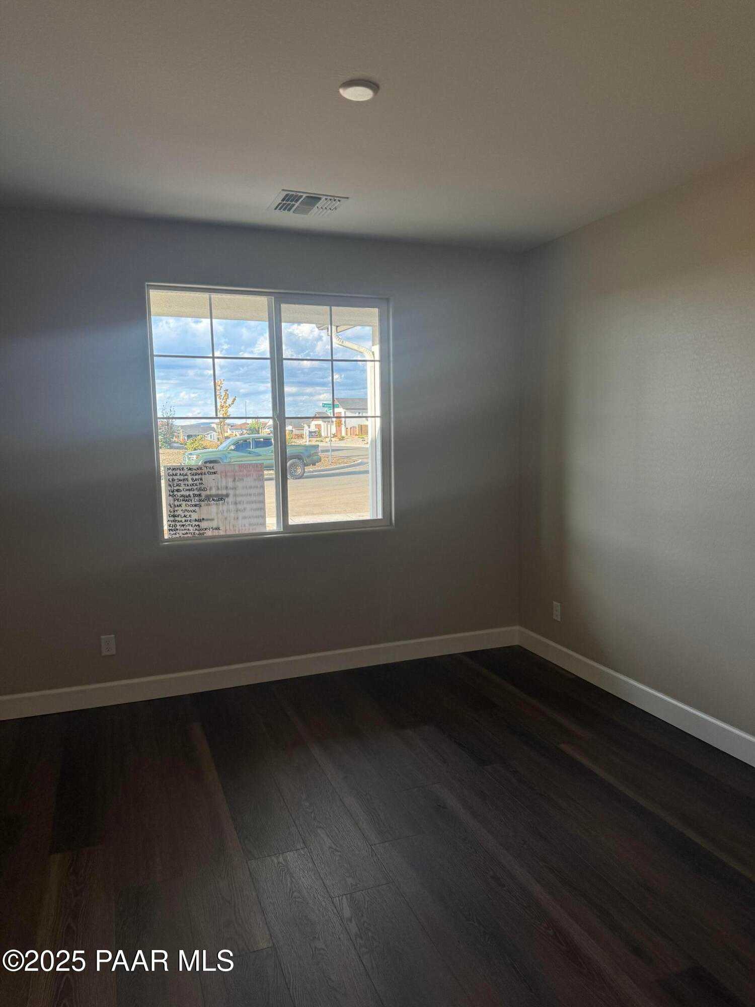 Bright bedroom featuring hardwood floors, neutral walls, and large grid window with sunny outdoor view in Evermore Homes The Sunrise A, Prescott Valley, Arizona