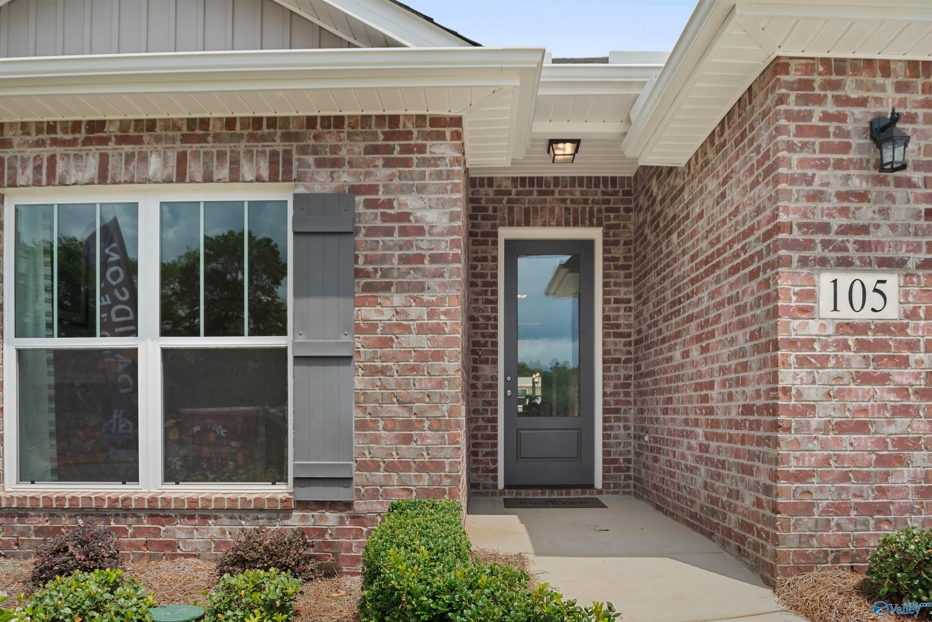 Brick single-story home exterior with covered entry, glass front door, large windows, and shrubs in Flint Meadows, New Market, Alabama