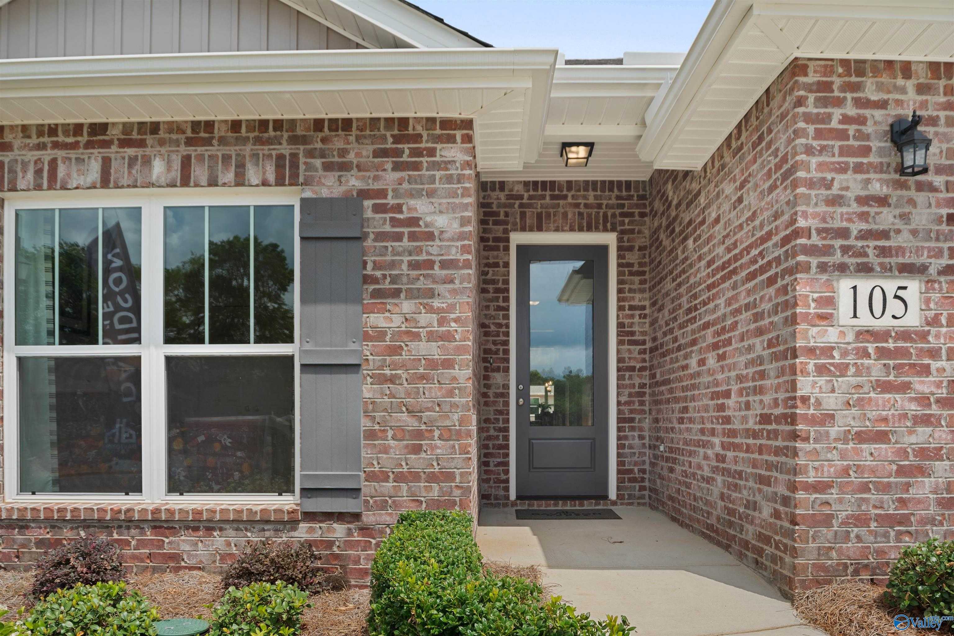 Brick single-story home exterior with covered entry, glass front door, large windows, and shrubs in Flint Meadows, New Market, Alabama