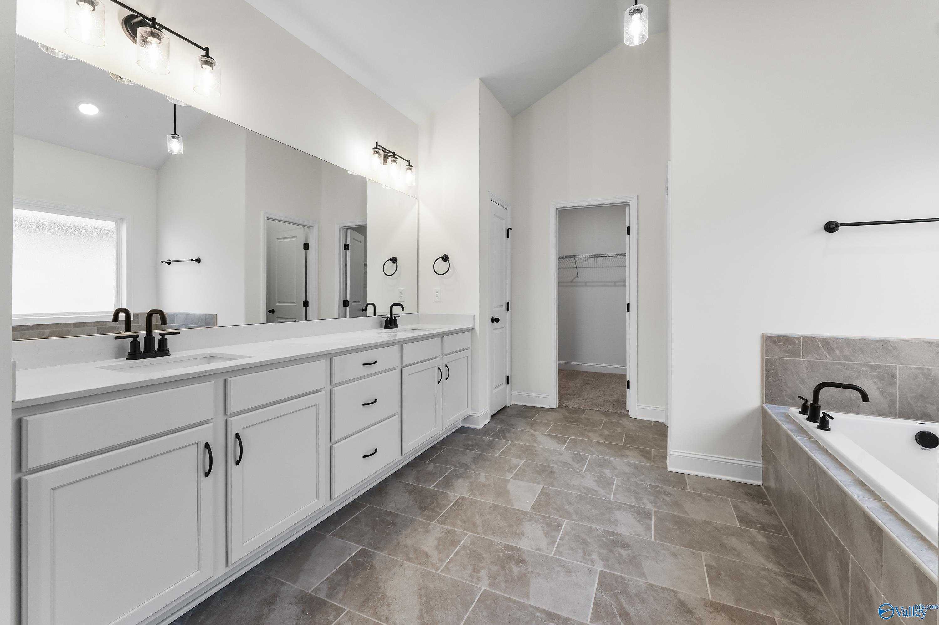 Modern master bathroom featuring double white vanity, freestanding tub, and tiled flooring in Davidson Homes The Finleigh, Harvest, Alabama