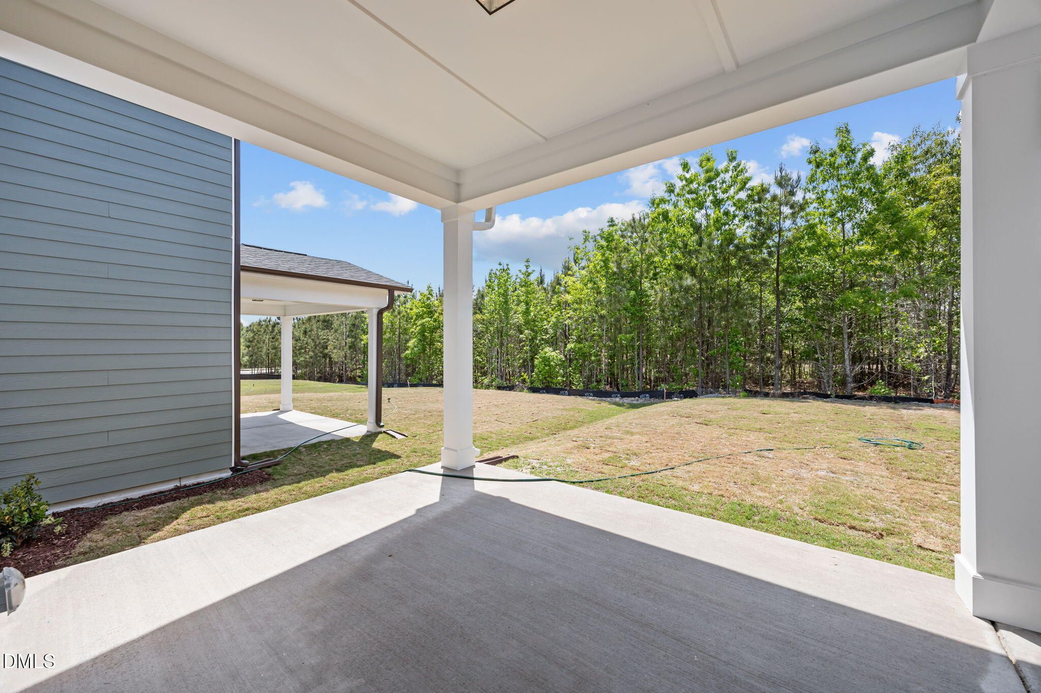 Covered porch with white columns on gray-sided 2-story home, overlooking wooded yard in Wendell Ridge, NC