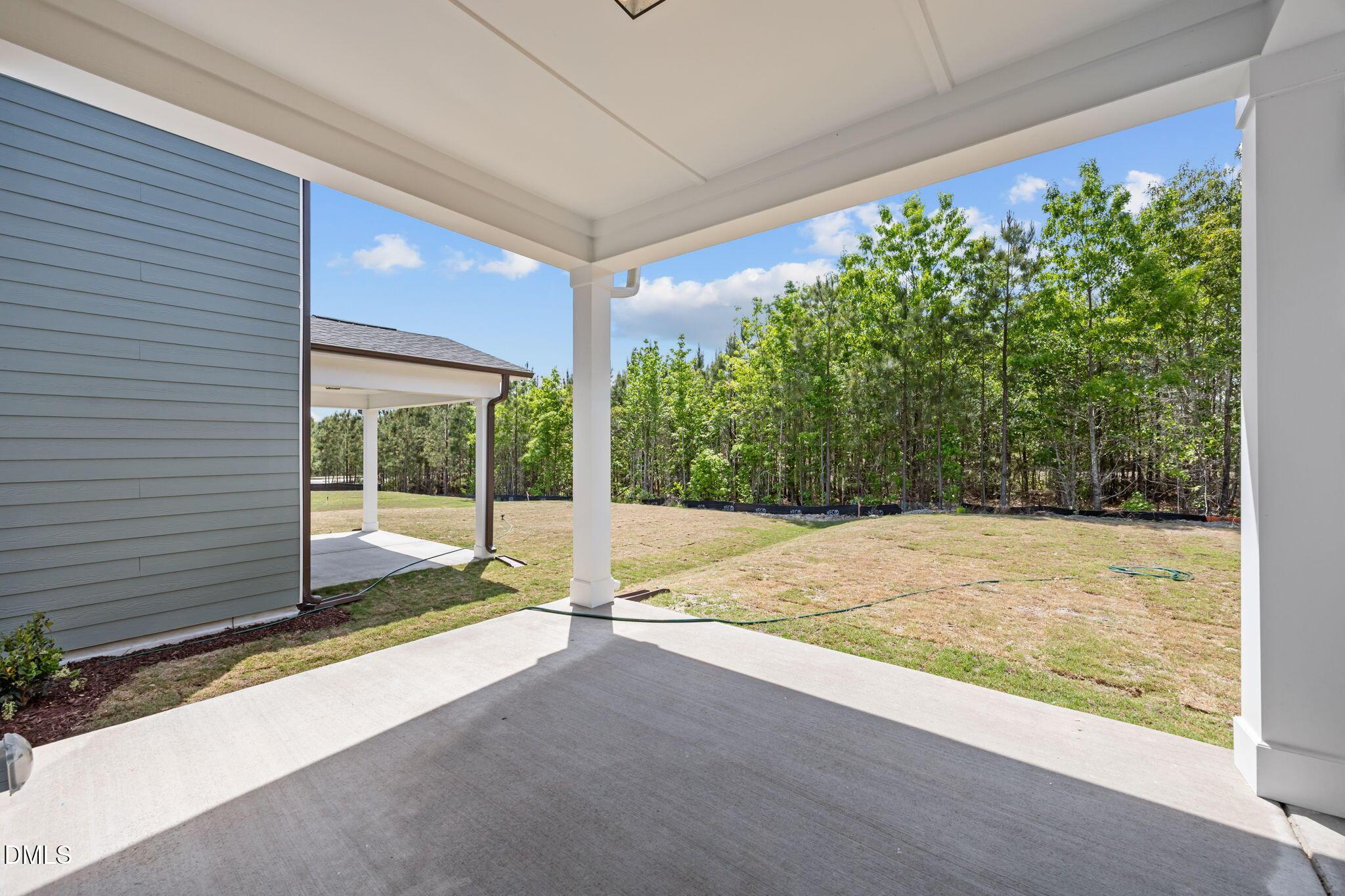 Covered porch with white columns on gray-sided 2-story home, overlooking wooded yard in Wendell Ridge, NC