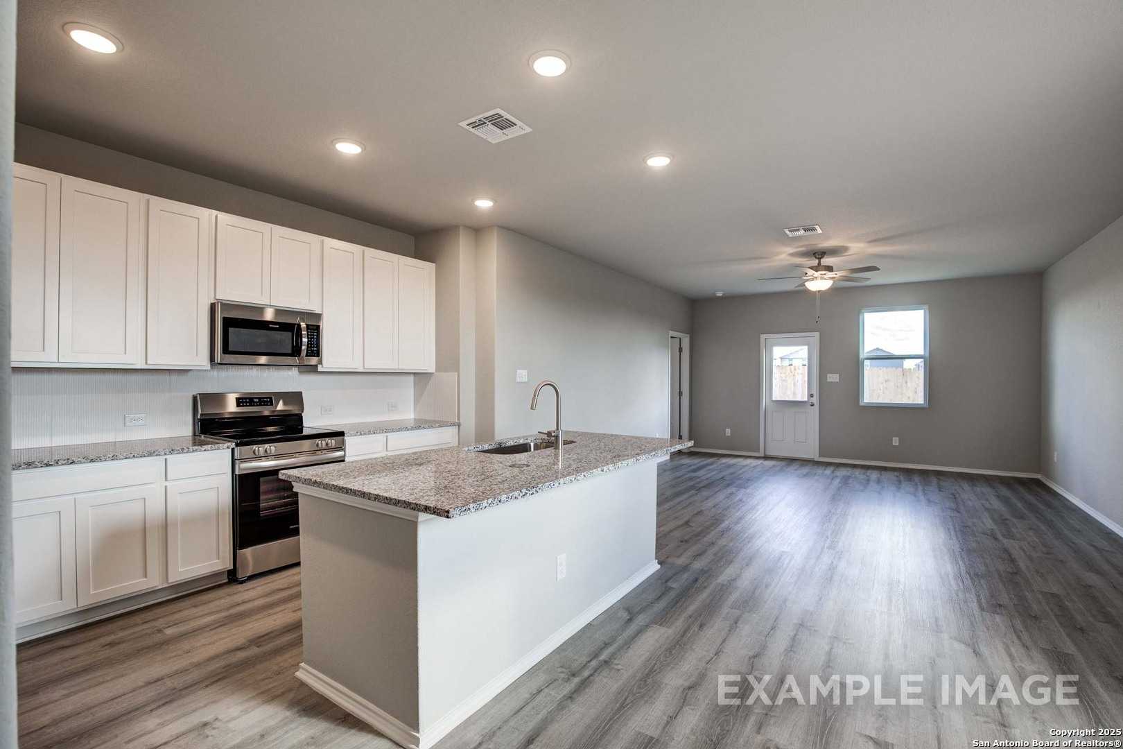 Modern open-concept kitchen with white shaker cabinets, granite island, stainless appliances in Davidson Homes The Blanco C, San Antonio