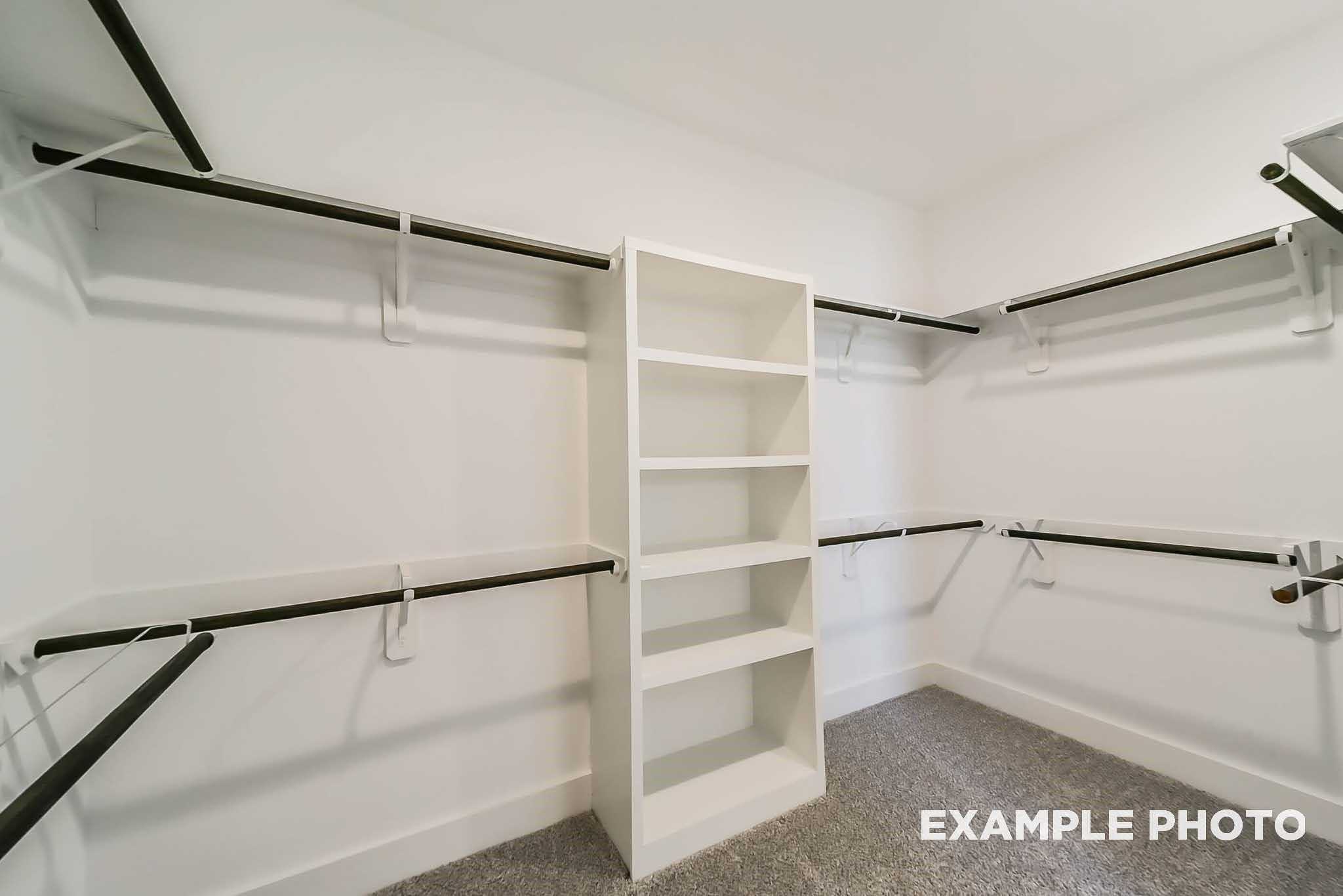 Spacious walk-in closet with white built-in shelves and hanging rods on carpet in The Philip C master suite, Davidson Homes, Rosharon, Texas