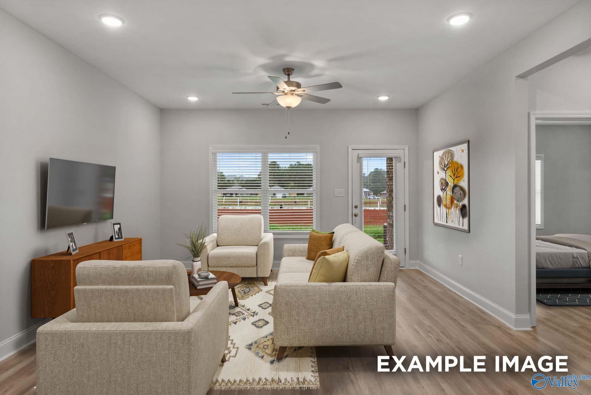 Cozy living room with beige sofa, armchairs, mounted TV, ceiling fan, and backyard view in Davidson Homes Cumberland B, Decatur, Alabama