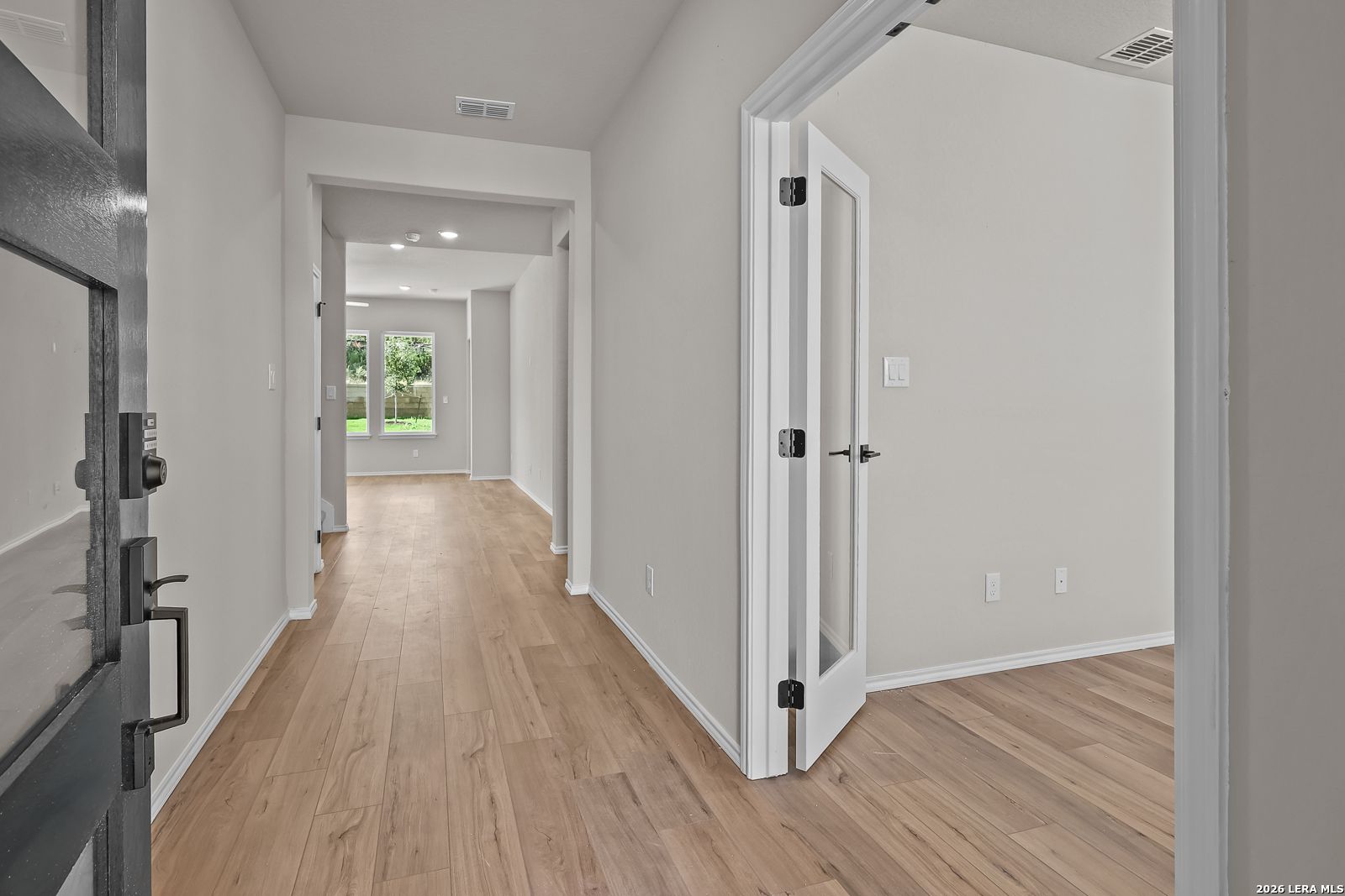 Bright entryway with wood-look flooring, glass-panel study door, and black front door in Davidson Homes Sequoia C, San Antonio