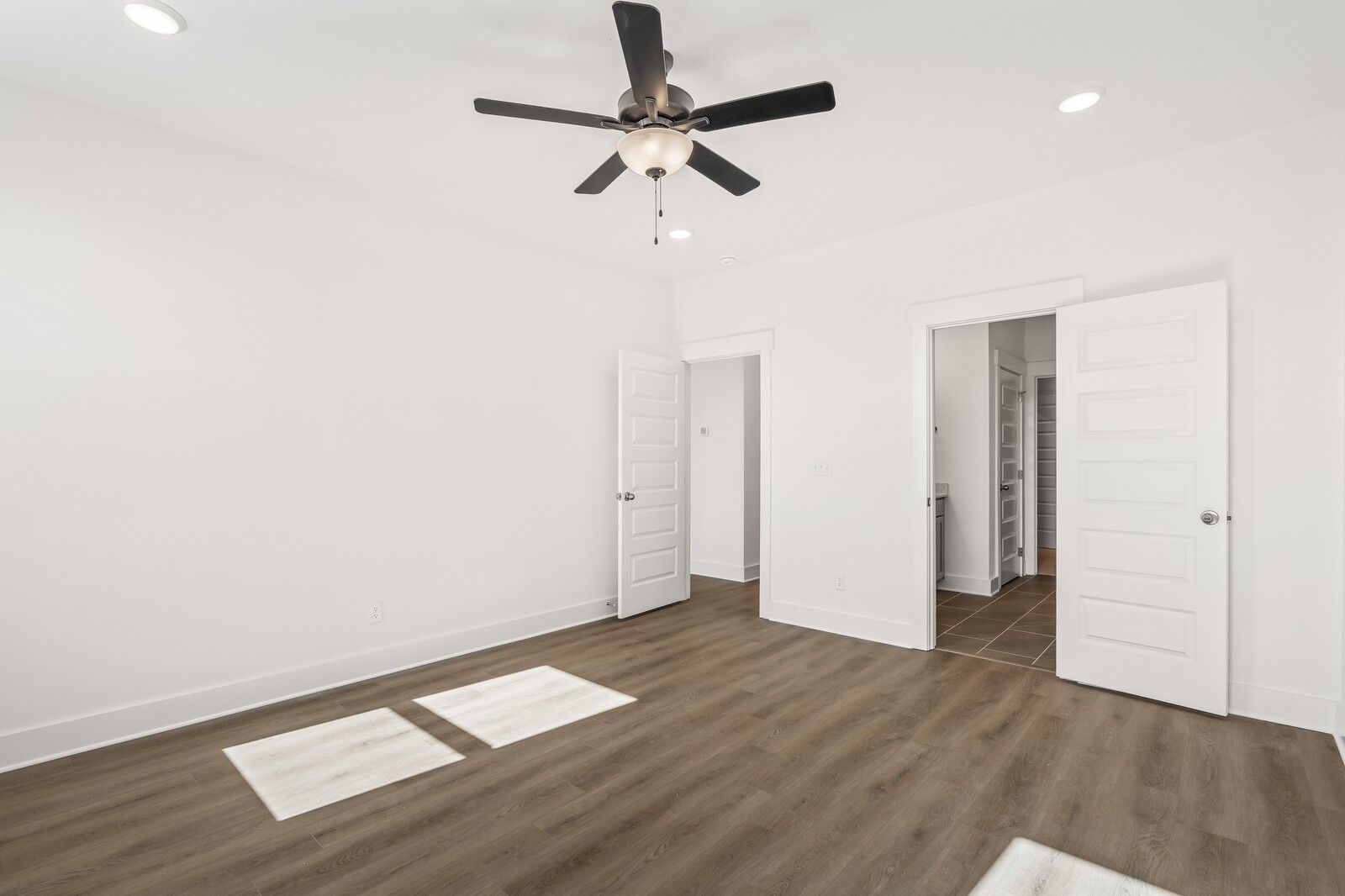 Bright bedroom with ceiling fan, laminate wood flooring, and doors to closet and bath in Davidson Homes The Ash A, Gallatin, TN