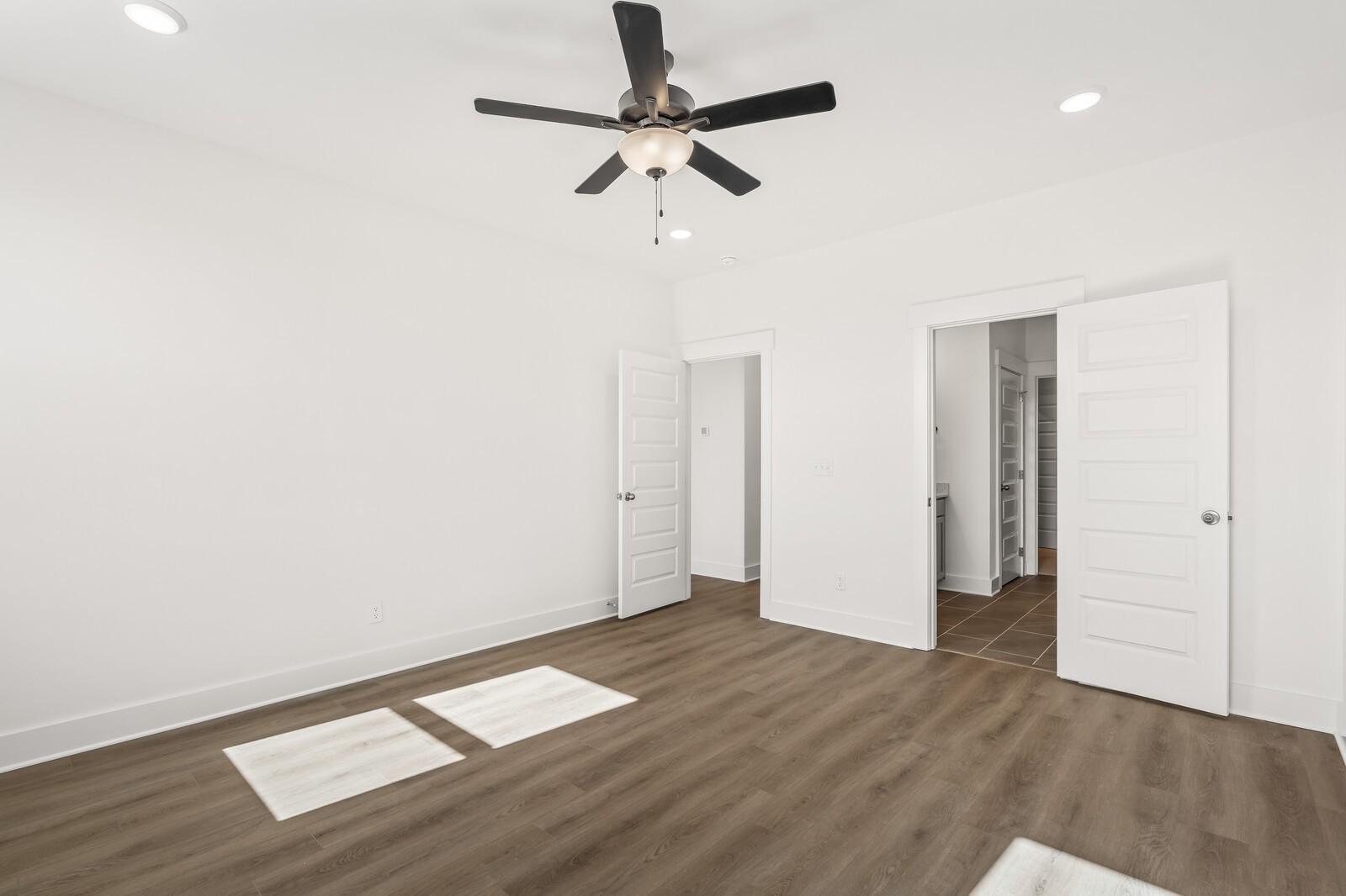 Bright bedroom with ceiling fan, laminate wood flooring, and doors to closet and bath in Davidson Homes The Ash A, Gallatin, TN