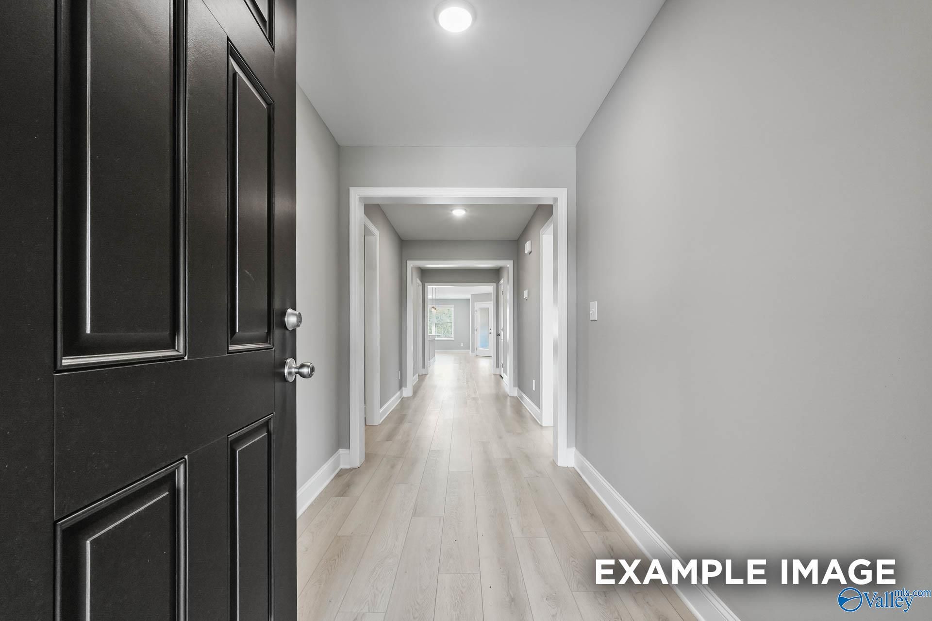 Long hallway with light oak floors, gray walls, and white trim from open black front door in Davidson Homes The Everett B, Toney, Alabama