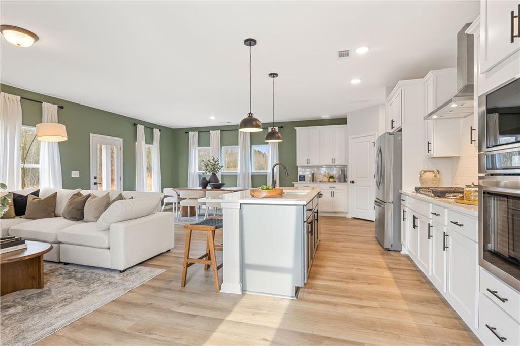 Open-concept kitchen and living area with white cabinets and green accent walls in The Rabun B home at The Bluffs, Canton.