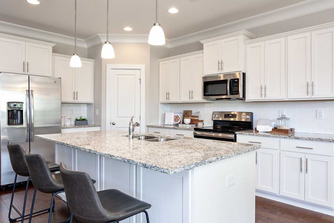 Modern kitchen in The Rockford by Davidson Homes featuring white cabinets, granite island with sink, stainless appliances, and pendant lights